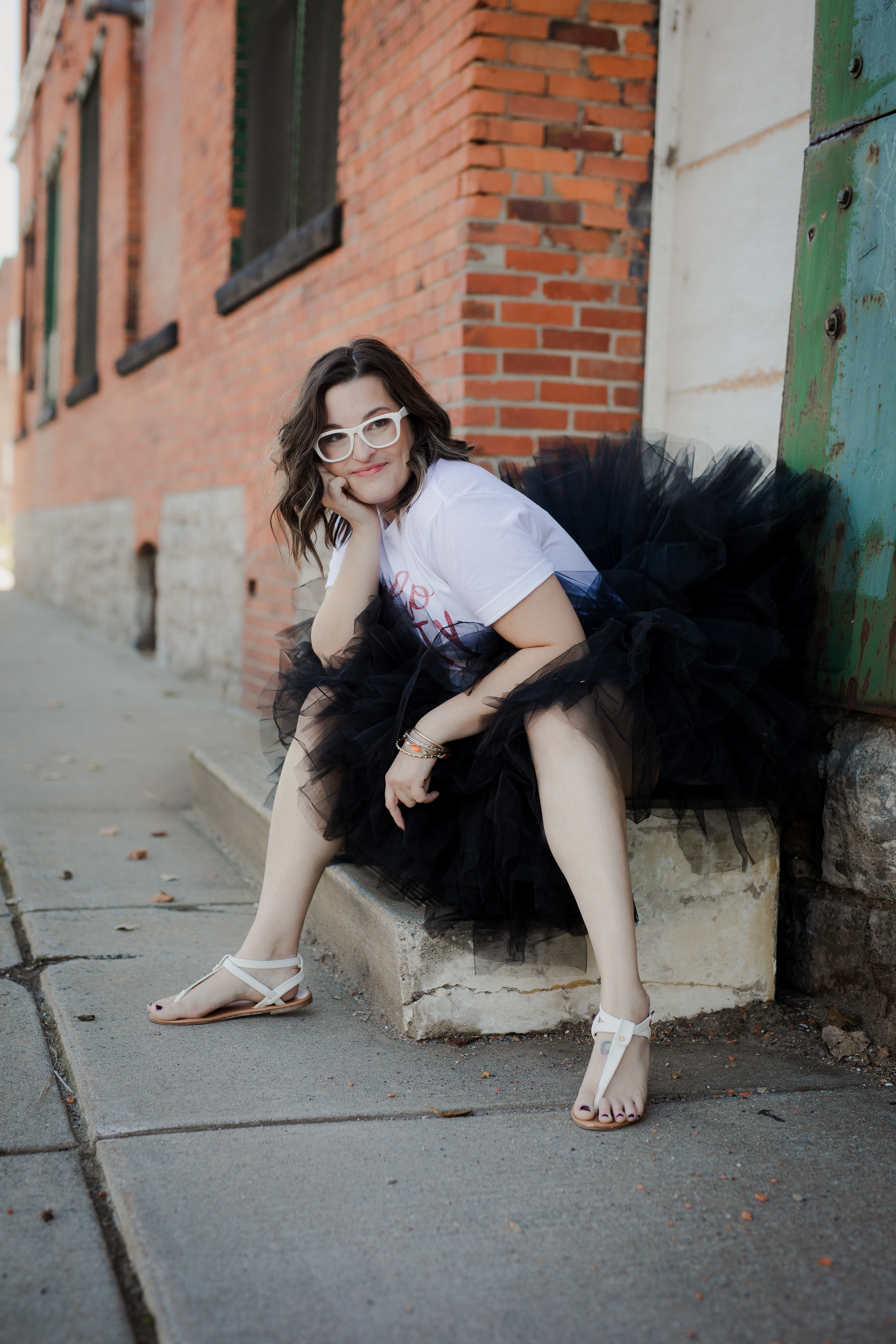 Woman wearing a “Hello Forty” shirt and black tulle skirt posing outdoors against a brick wall for a birthday milestone photoshoot. Woman wearing a “Hello Forty” shirt and black tulle skirt posing outdoors against a brick wall for a birthday milestone photoshoot.