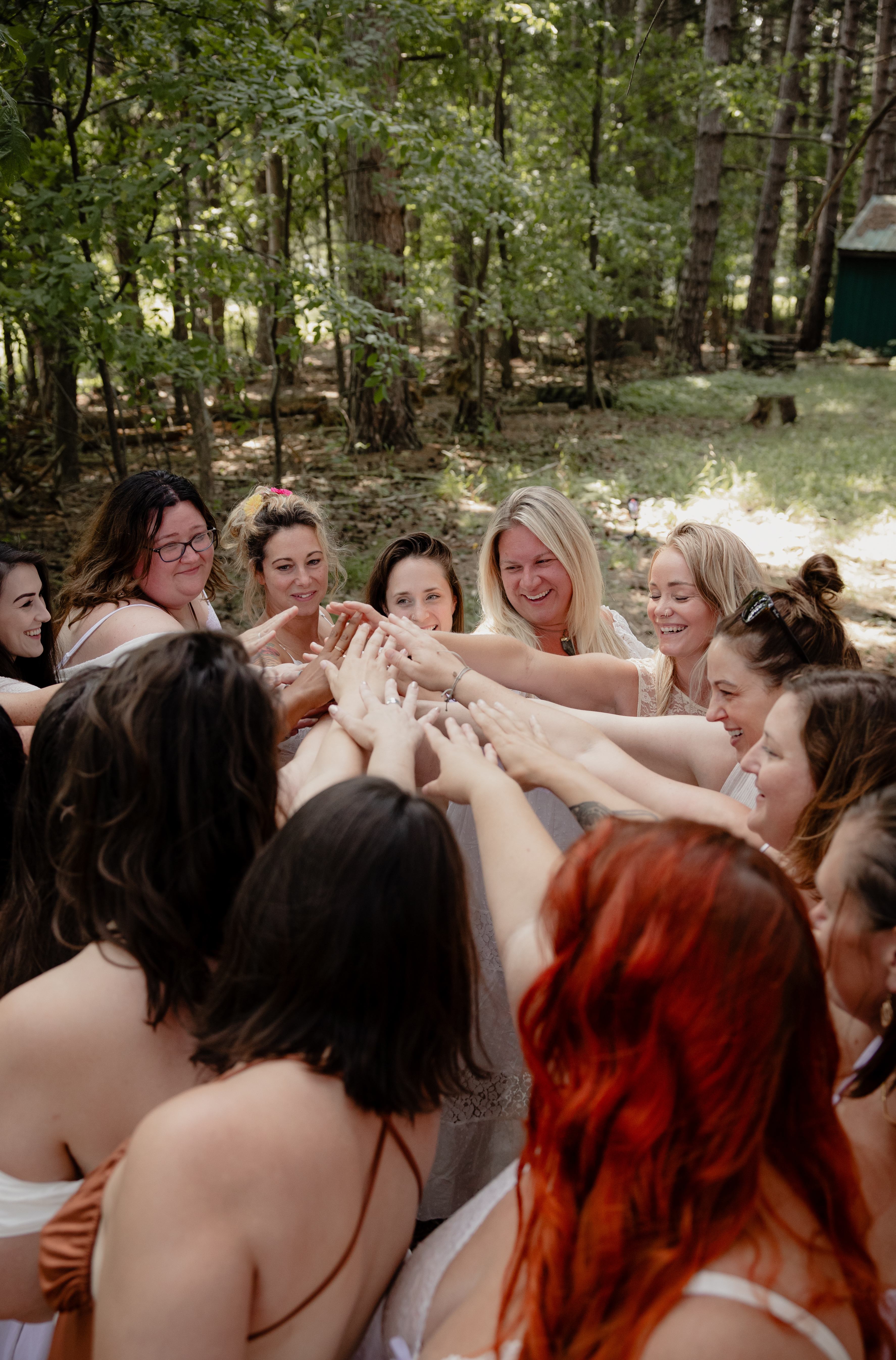 Women raising their hands together in a circle during a forest boudoir empowerment session.