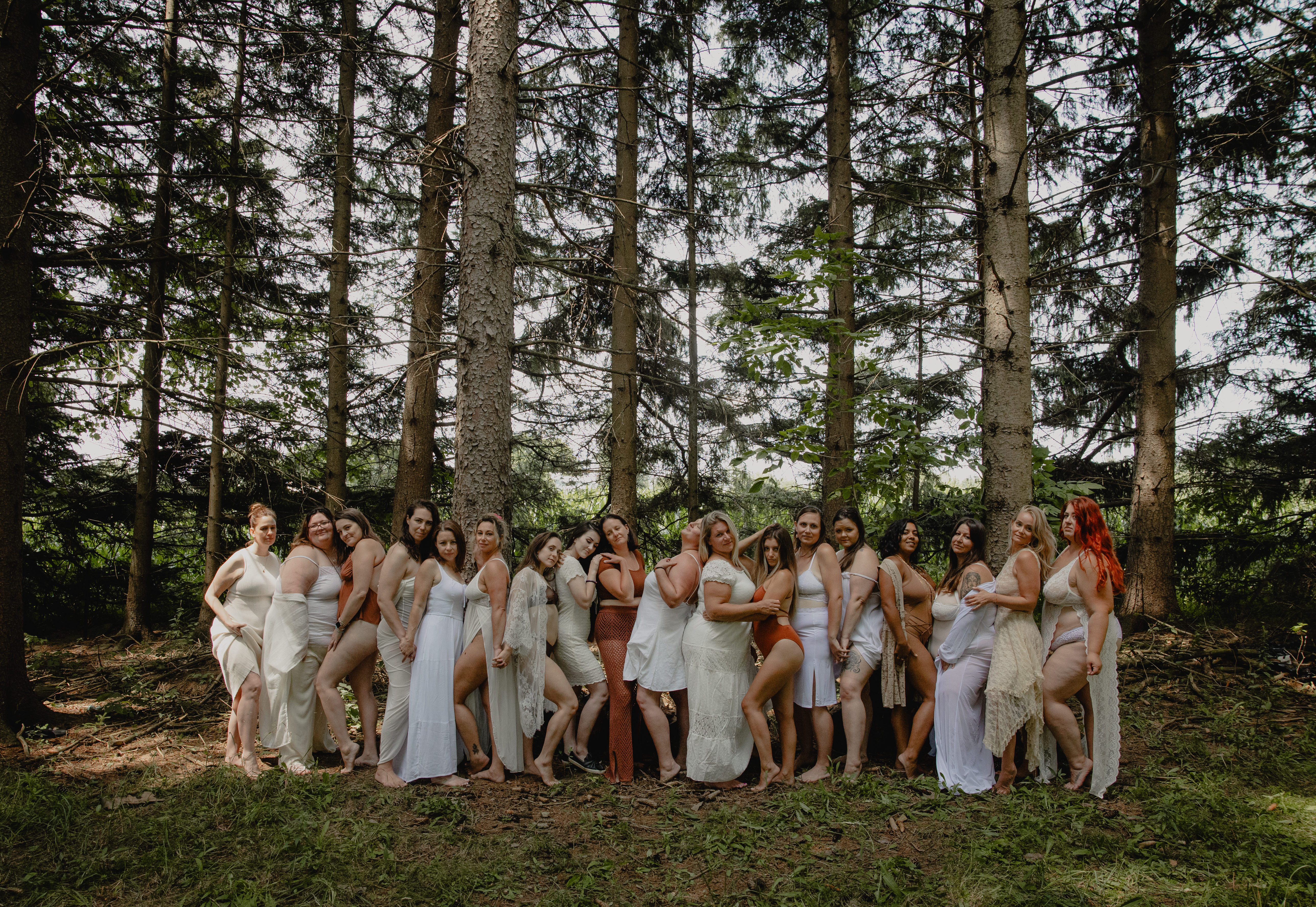 Large group of women posing together in a woodland setting for a boudoir event.