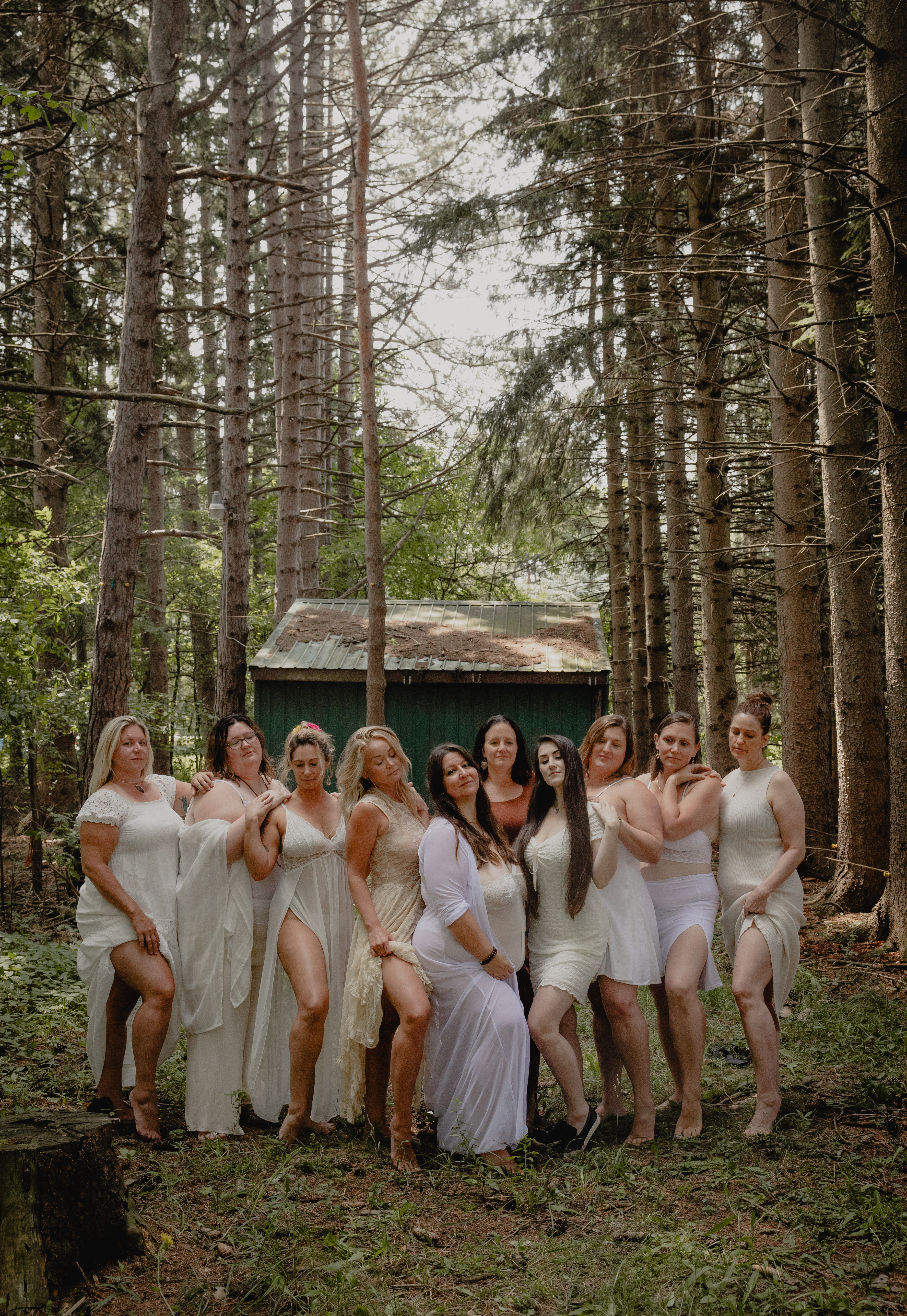 Group of women in white dresses gathered in a forest during a group boudoir photoshoot.