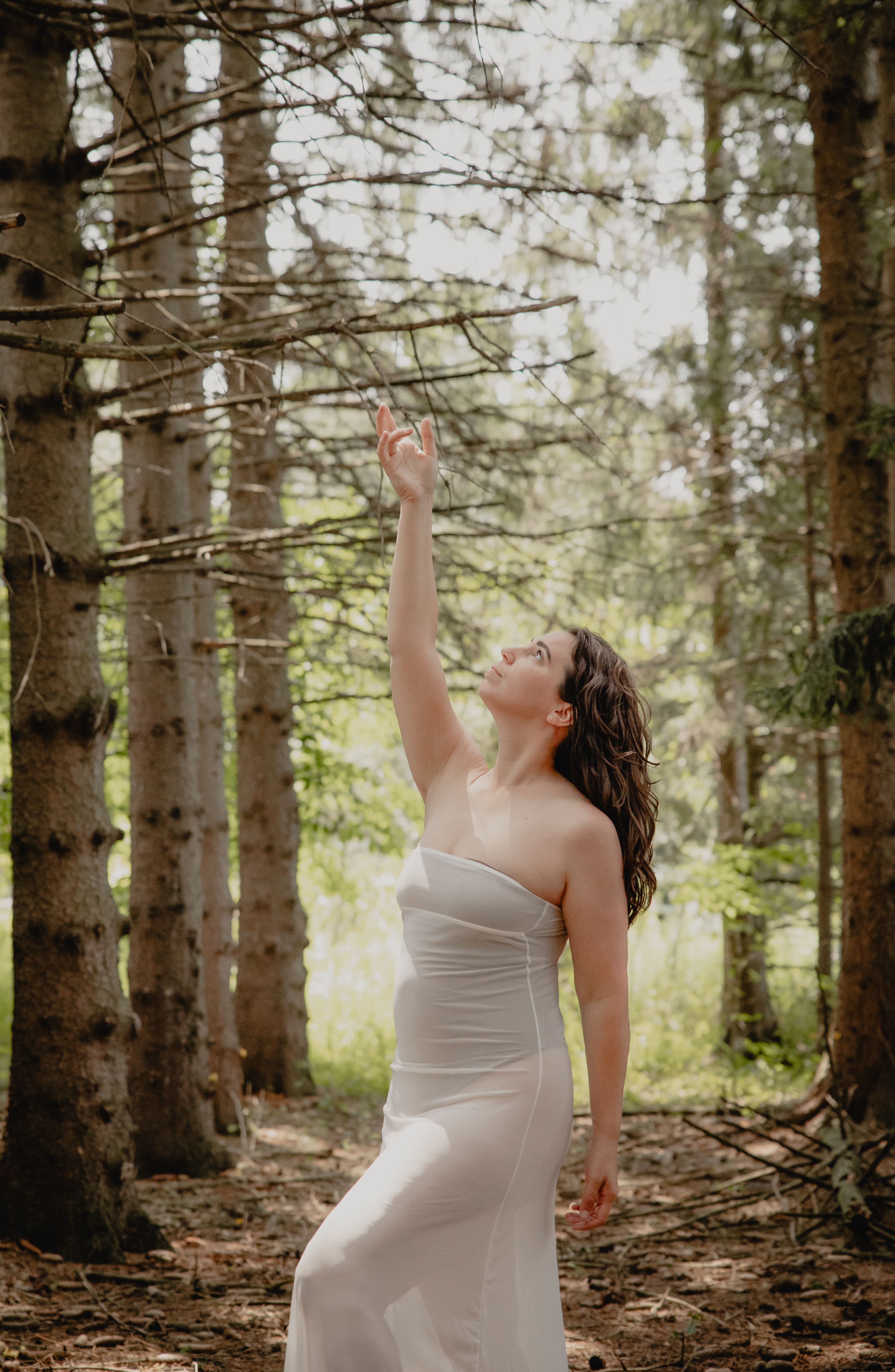 Woman reaching up toward sunlight in a forest during an outdoor boudoir photoshoot.