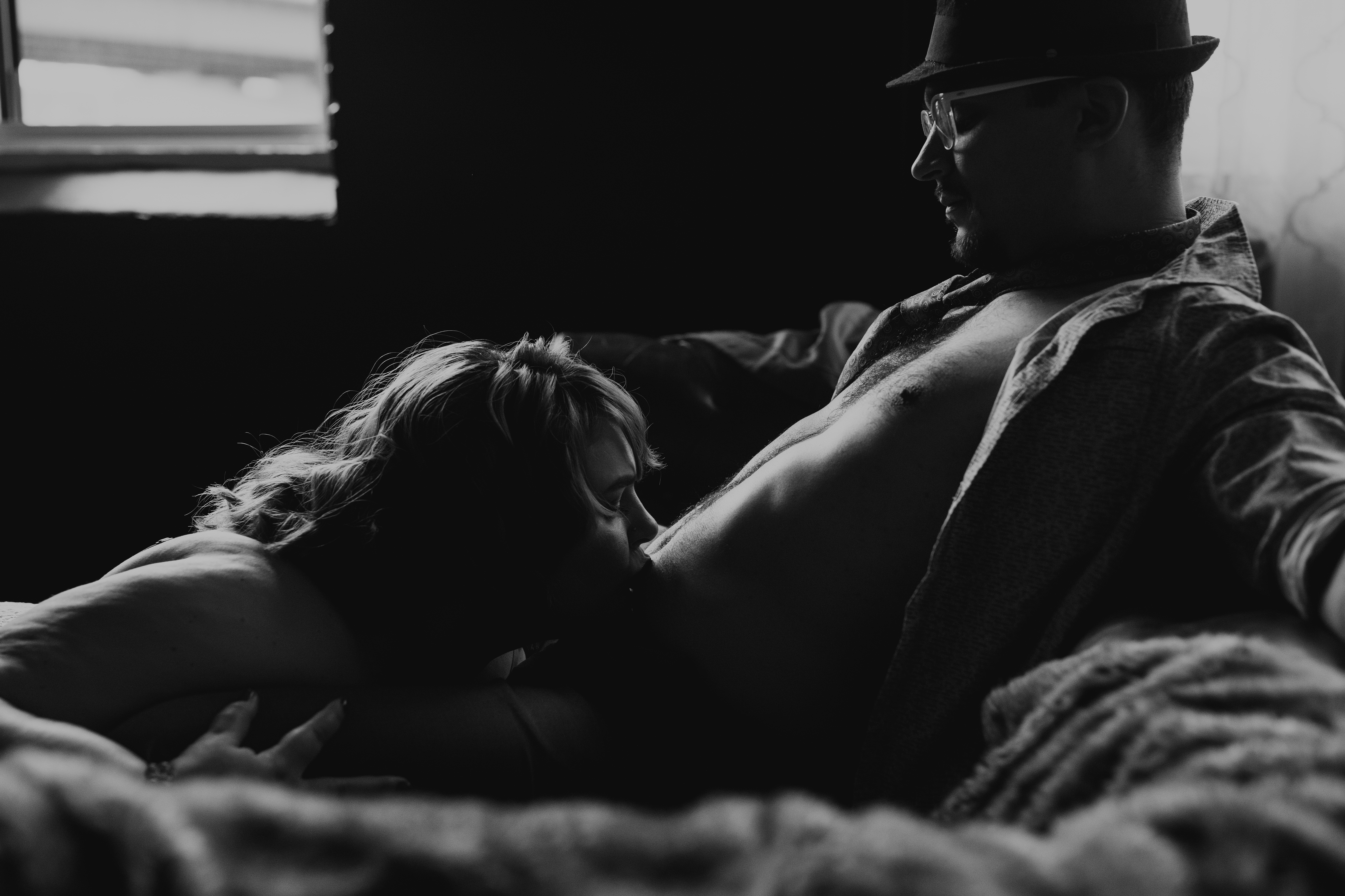 Black and white boudoir photo of a couple embracing in soft window light.