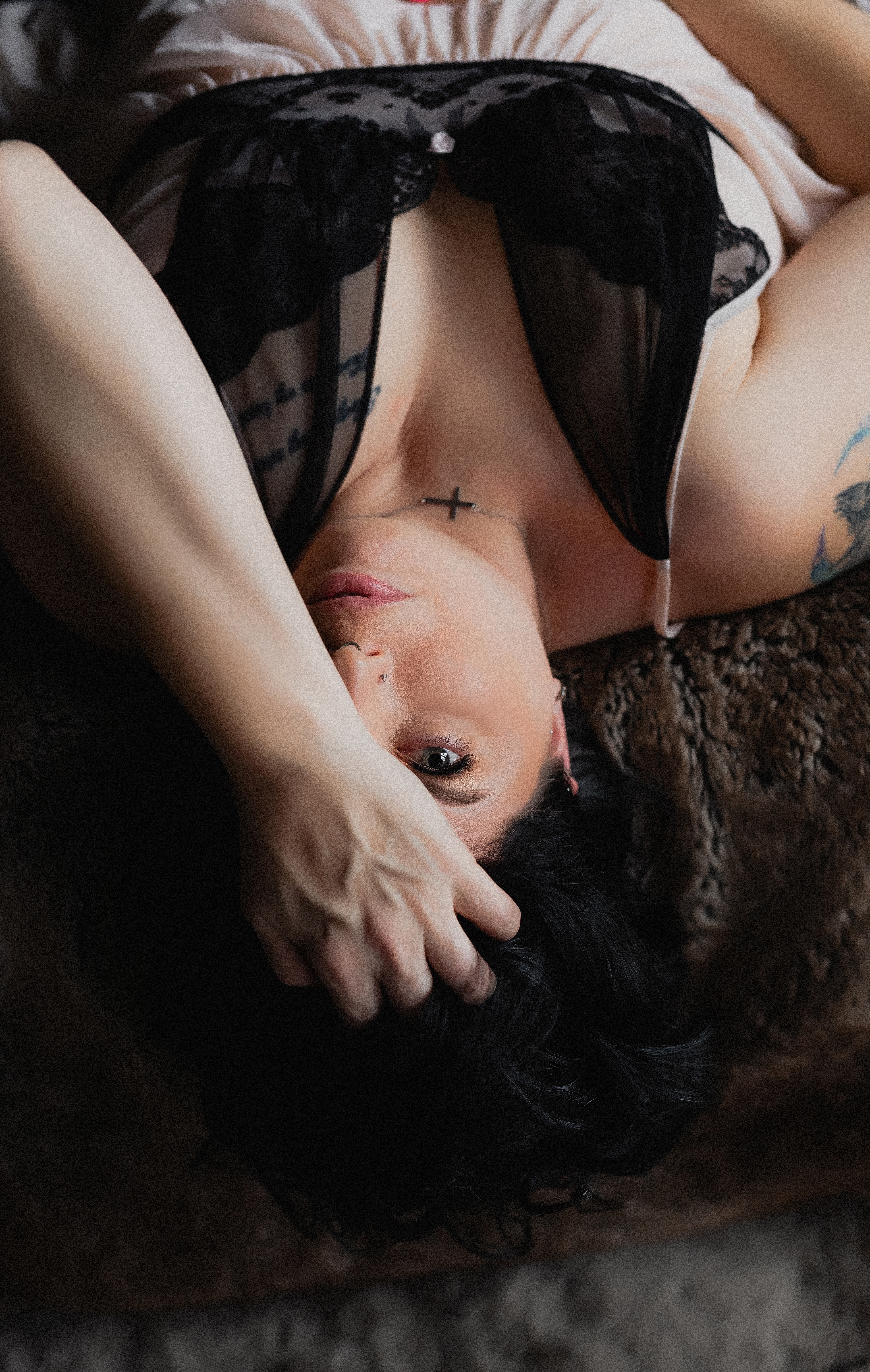 Boudoir portrait of a woman in black lingerie lying on a bed in soft, moody lighting.