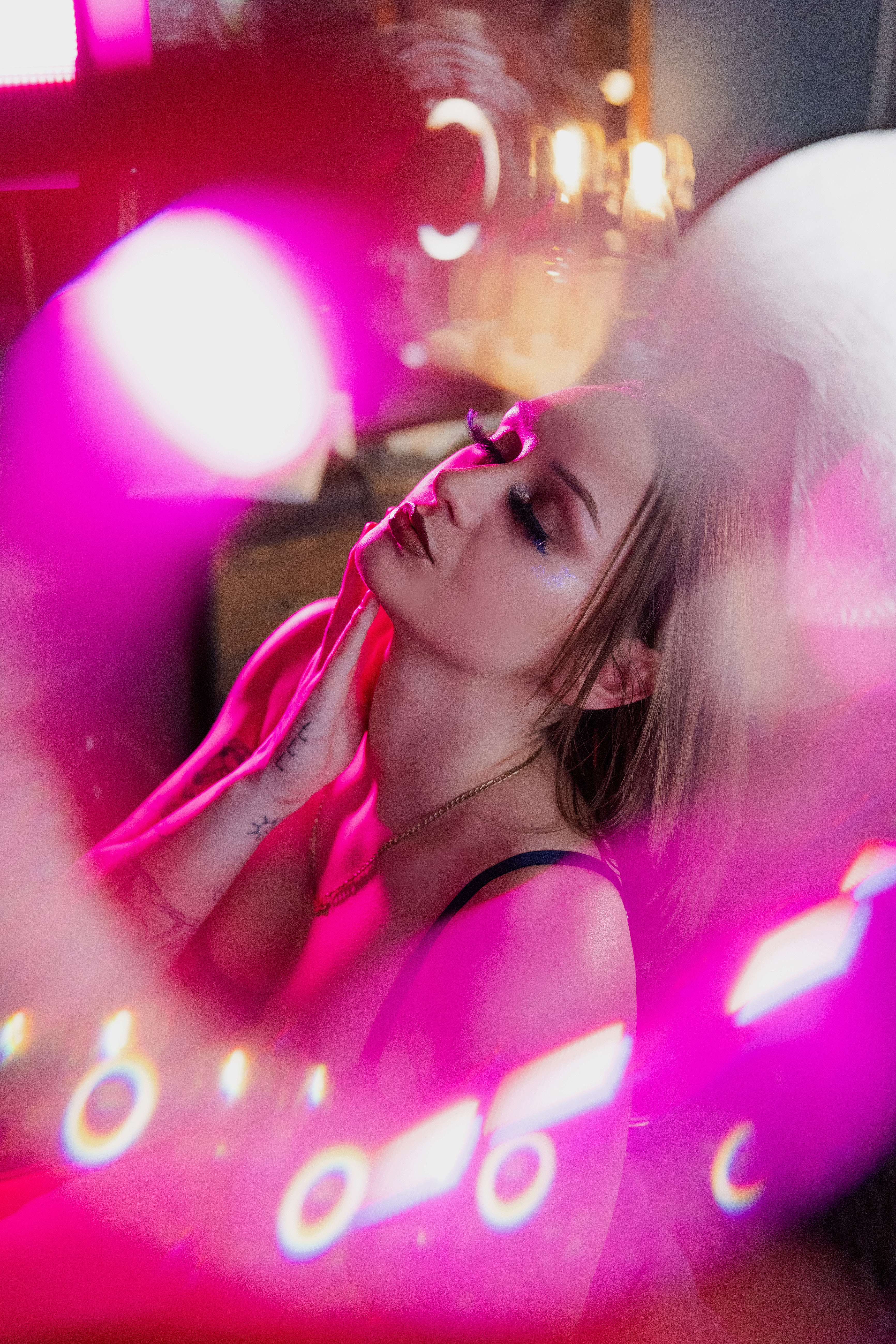 Close-up portrait of a woman in pink lighting during a glamorous boudoir session.