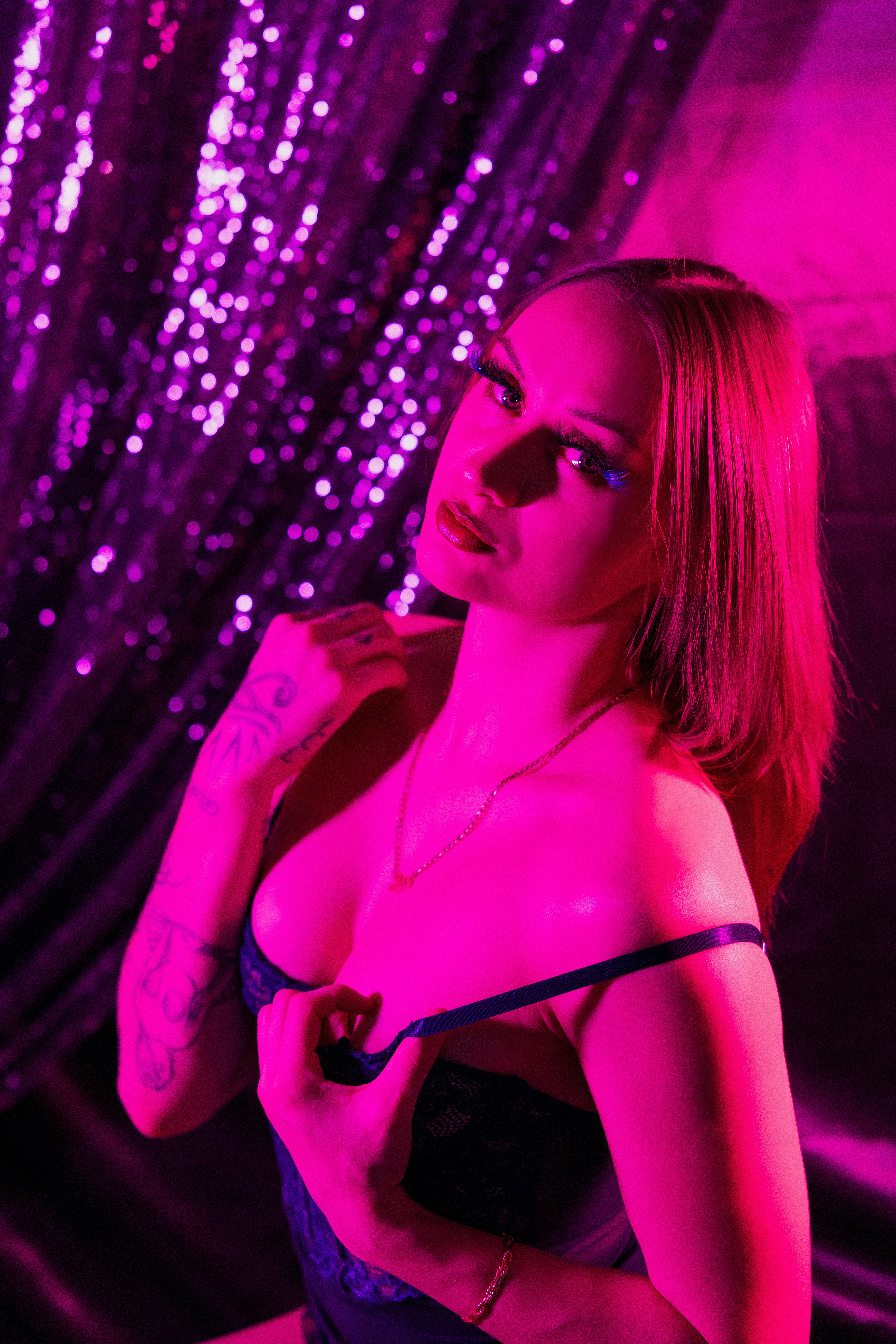 Boudoir portrait of a woman under pink neon lighting with shimmering backdrop.