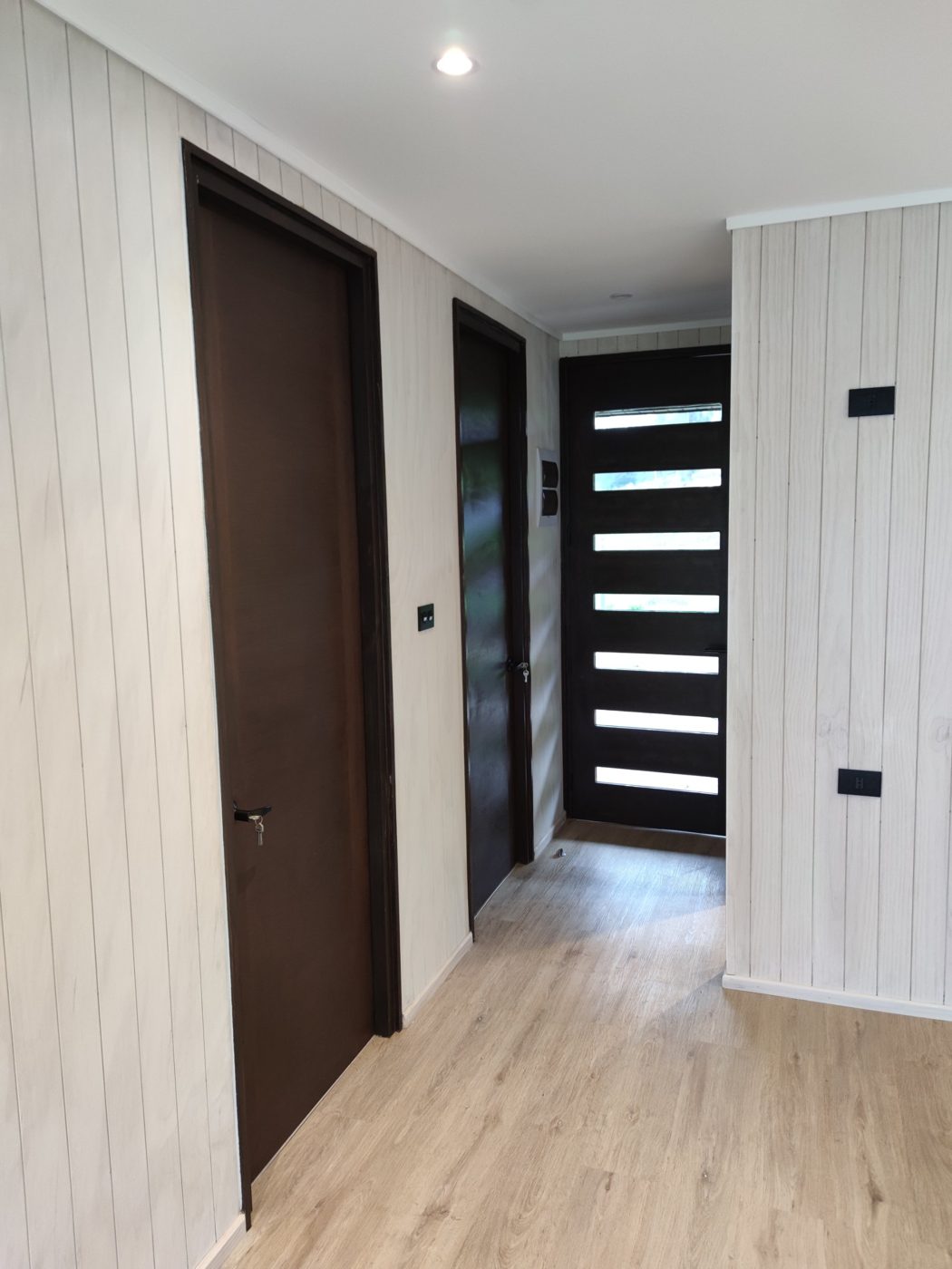 Pasillo interior de la casa de 398 m² en Quillón, con muros en terciado ranurado, puertas oscuras y piso flotante