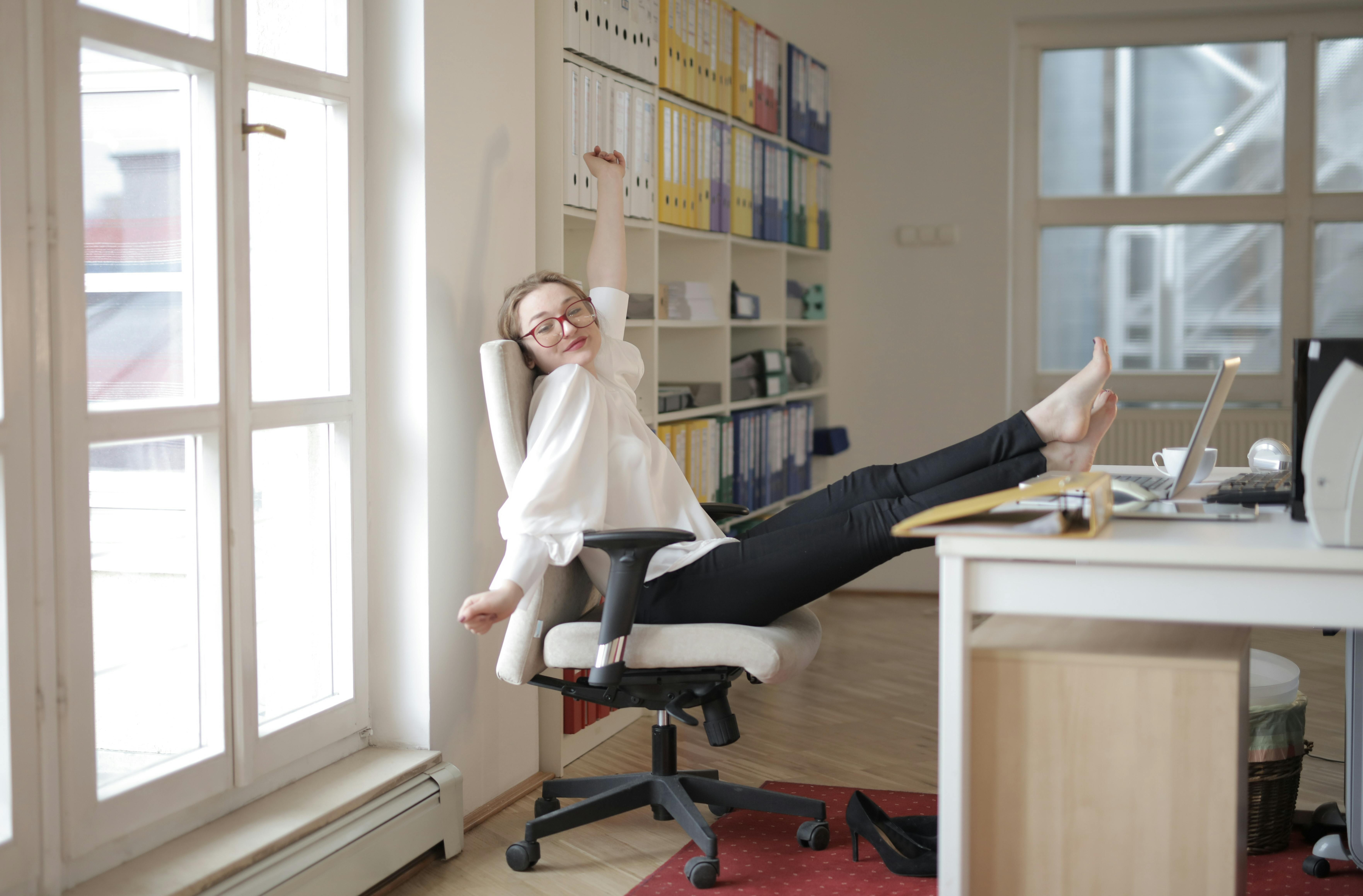 A calm woman sitting by an office window in natural light, symbolising spacious and sustainable business growth for soul-led coaches.