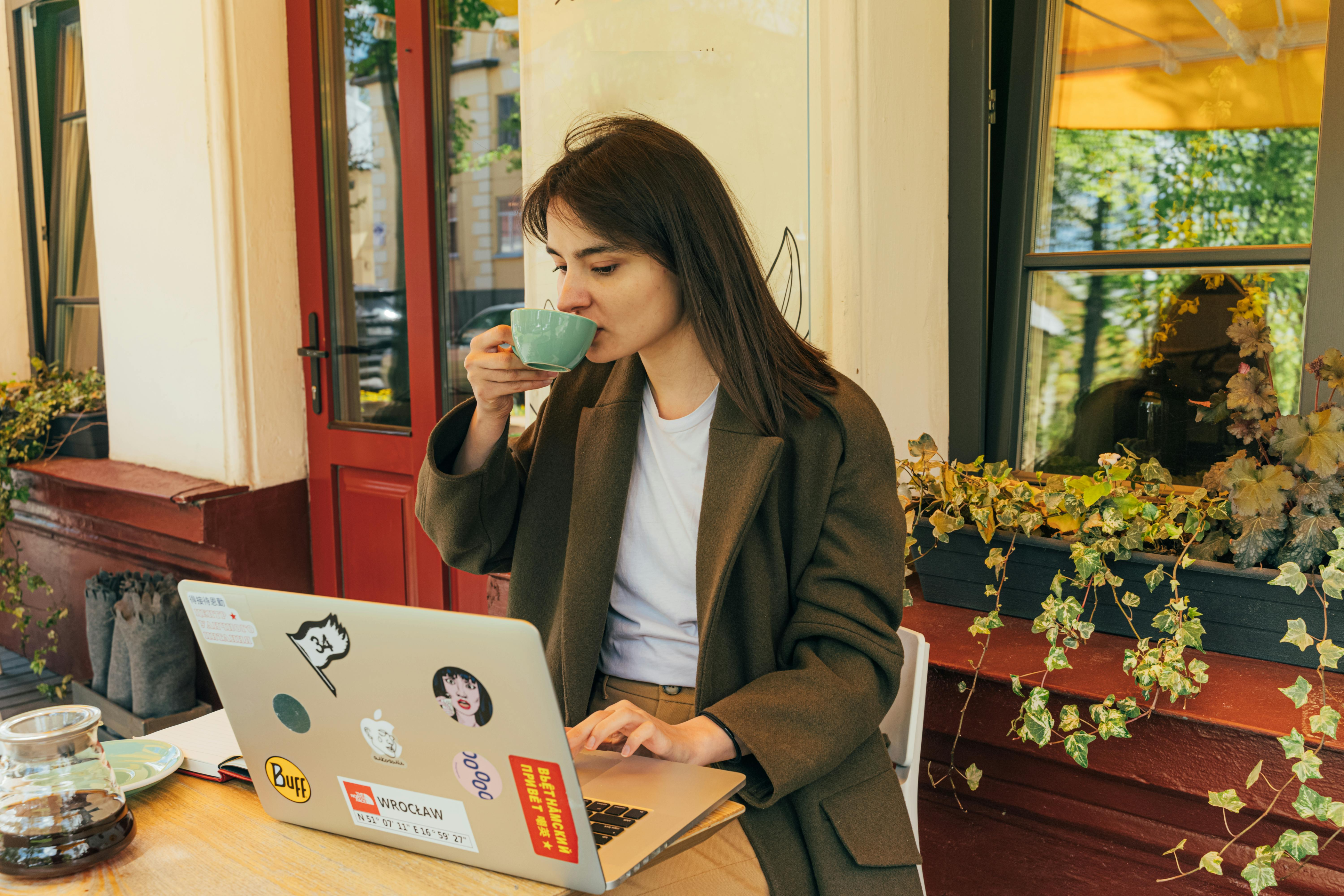 A woman working on her laptop with a notebook at a café, representing daily execution and sales process for spiritual entrepreneurs.