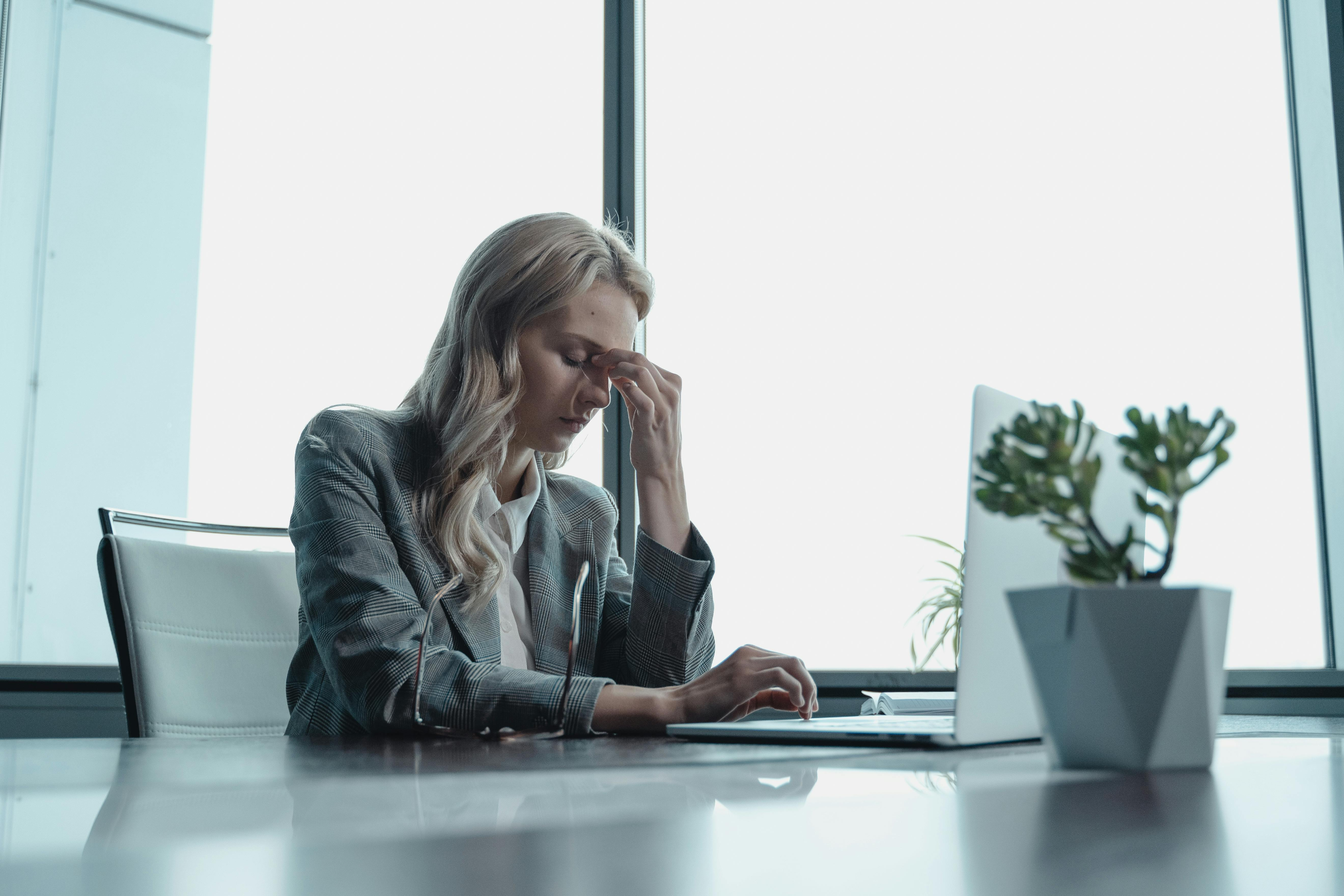 A woman sitting quietly at a desk, reflecting on the invisible ceiling that cultural conditioning placed on her ambition before she ever started her business.