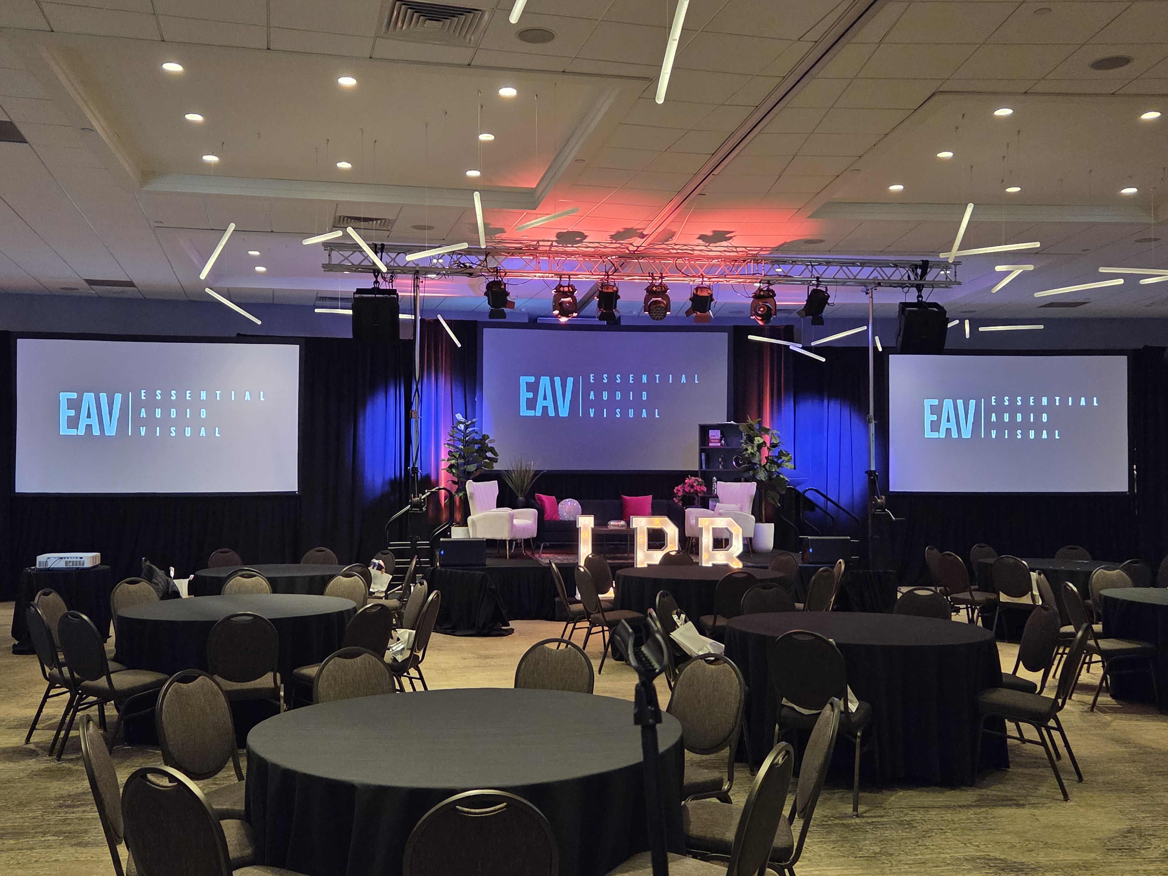 A branded Essential AV general session — three screens carrying the EAV mark above a staged ballroom of round tables.