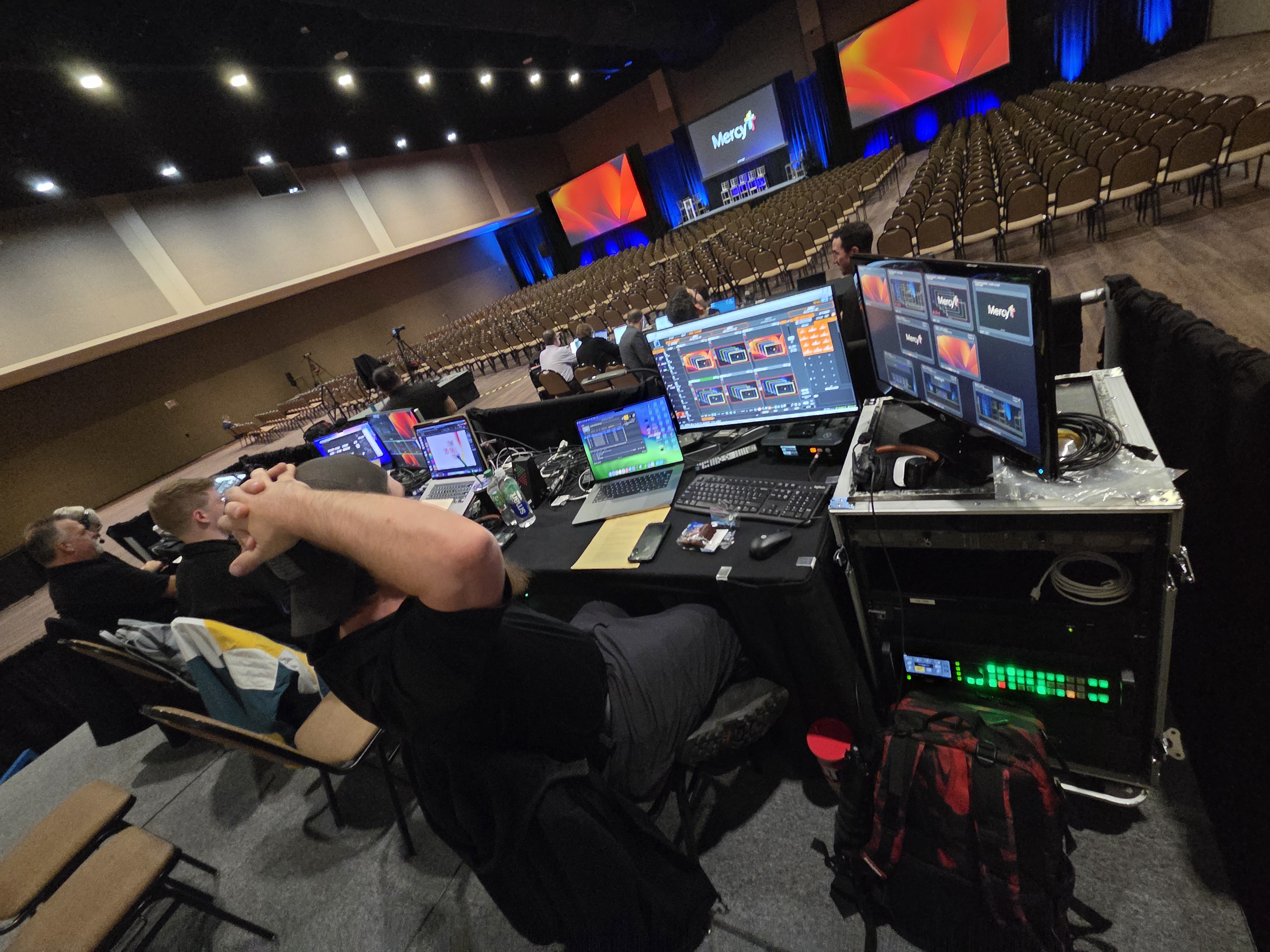 An Essential AV technician running the show from the front-of-house production desk — video switcher, audio console and confidence monitors.