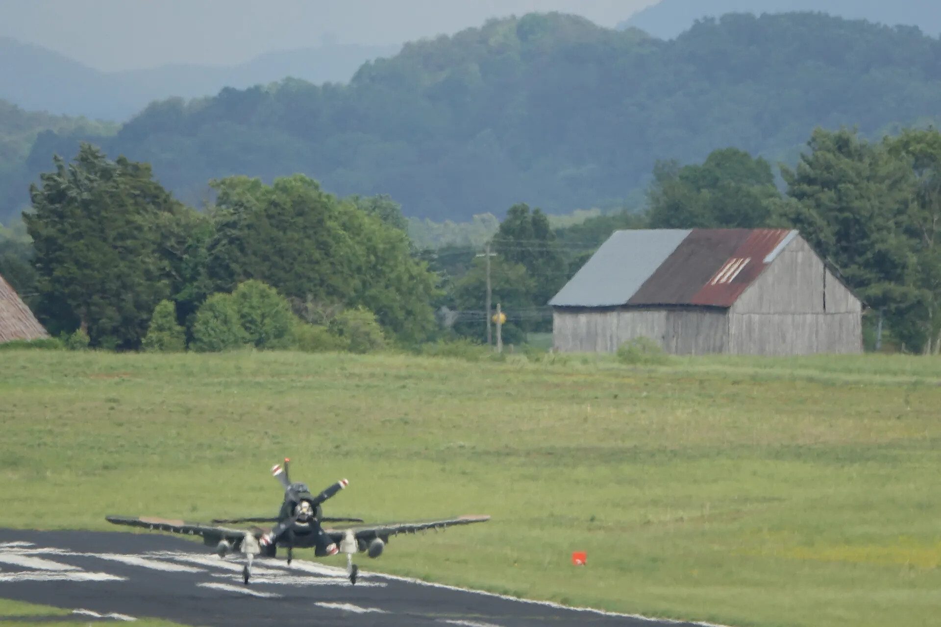 A-1 Skyraider on Runway, Head-On View with Rural Barn and Mountain Backdrop, May 2019