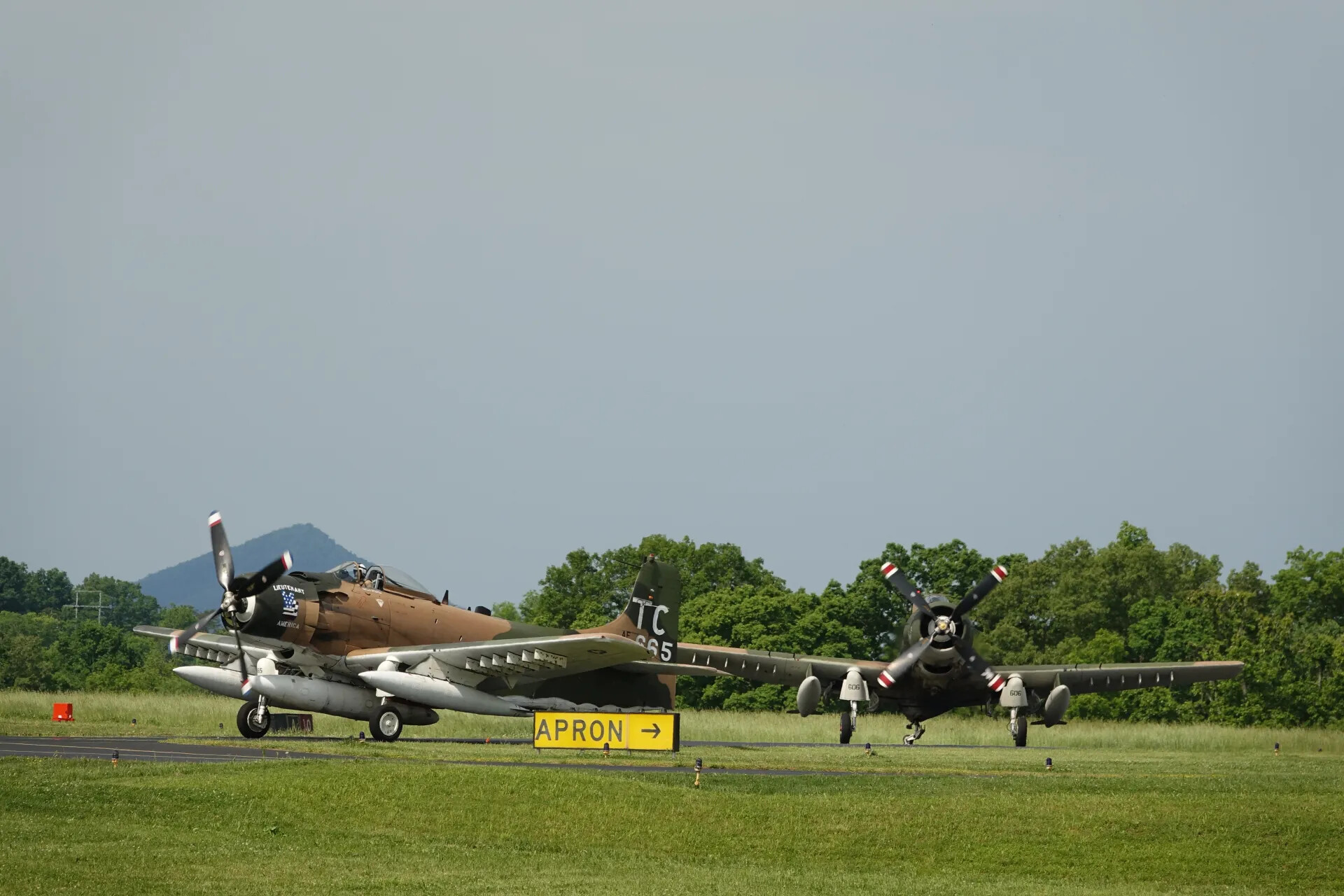 Two Douglas A-1 Skyraiders on Taxiway Near Apron Sign, Mountain Backdrop