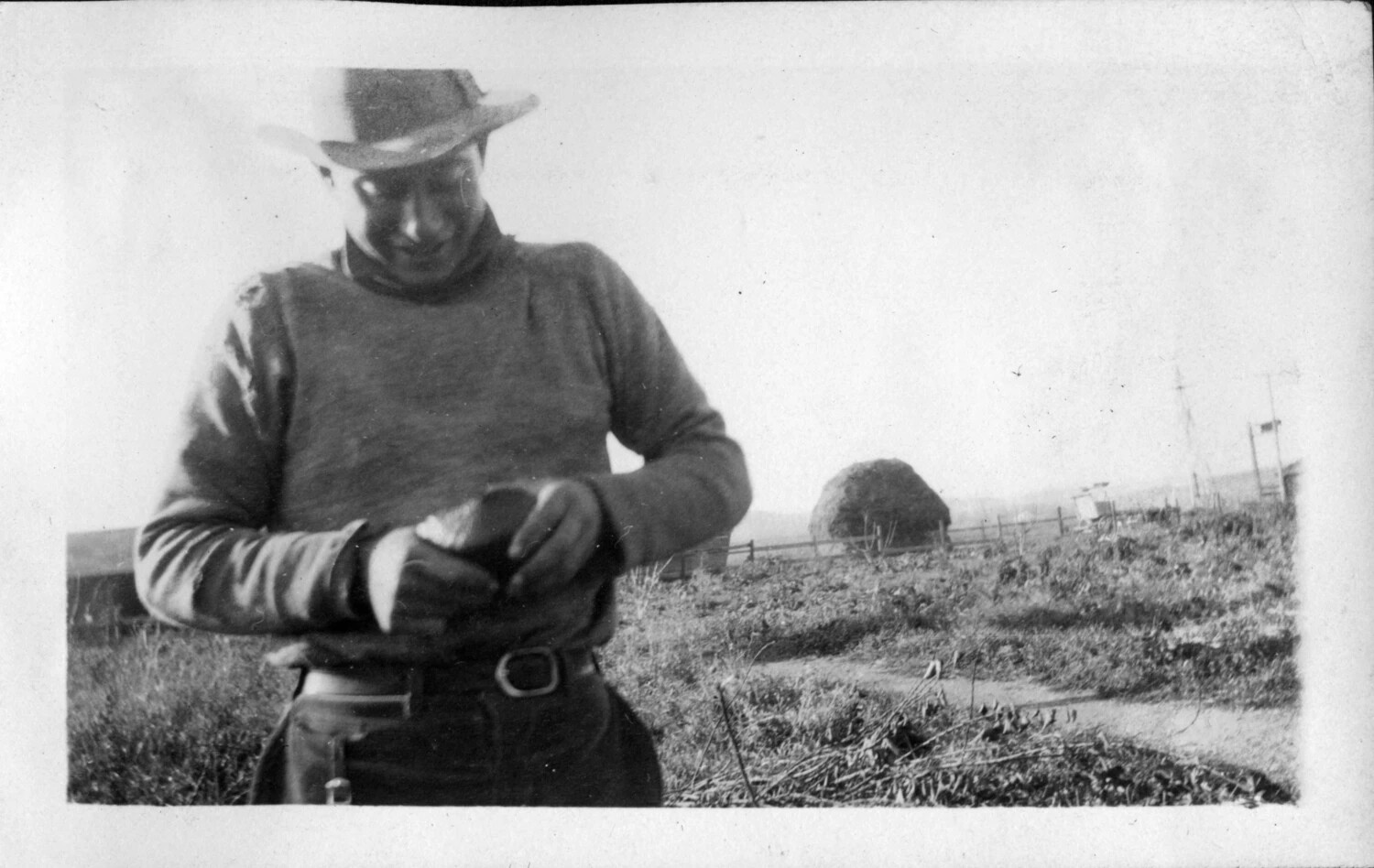 Man in Broad-Brimmed Hat and Sweater Handling an Object in an Open Field, c. 1920s