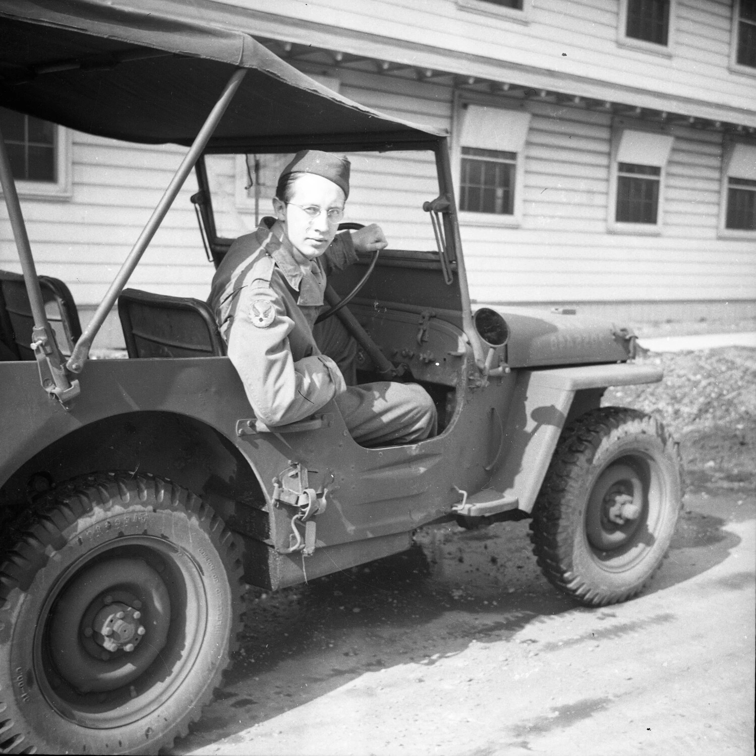 Serviceman Seated in WWII-Era Military Jeep Outside Barracks Building