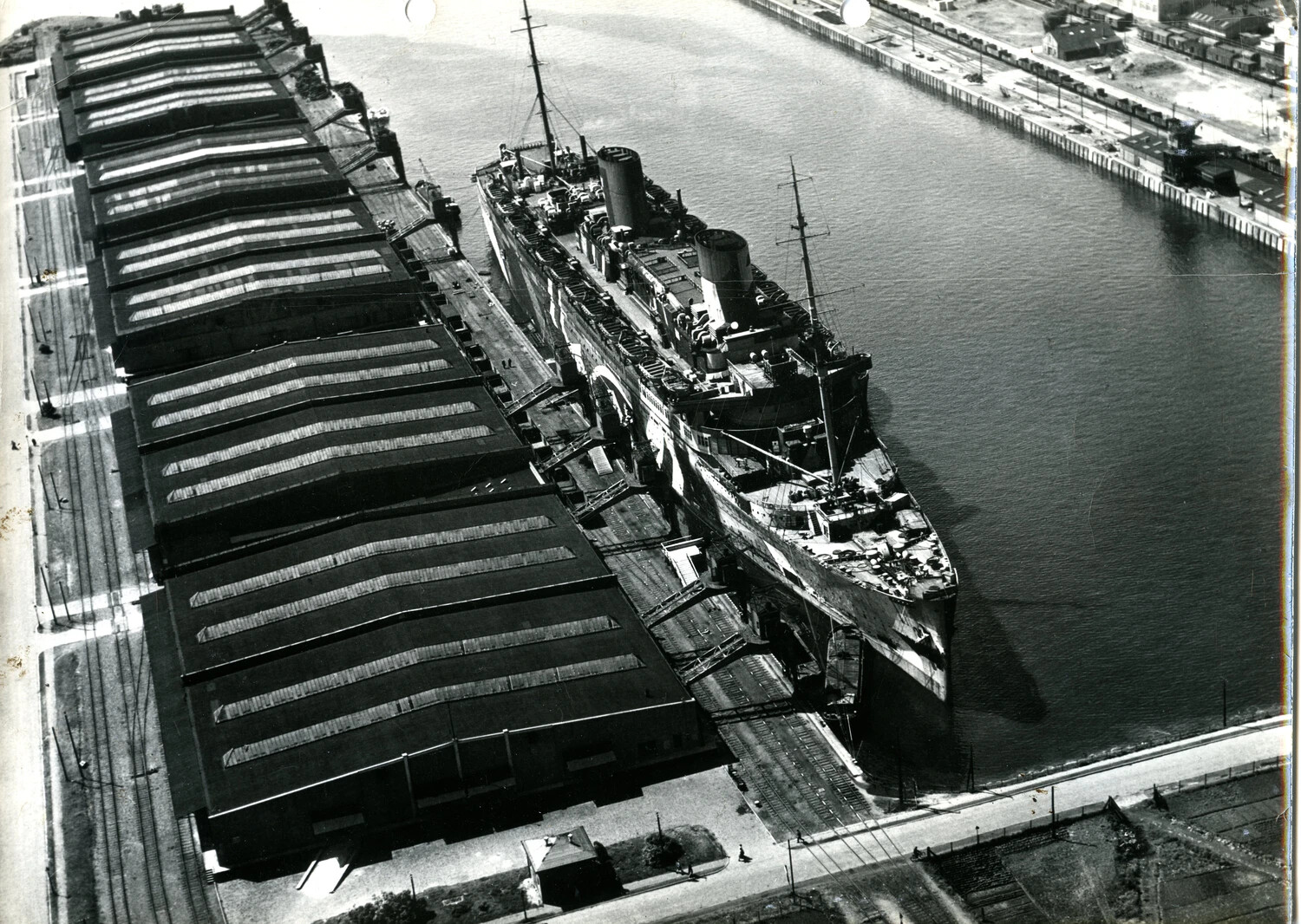 Aerial View of Ocean Liner/Troop Transport Moored at Port Facility, WWII Era