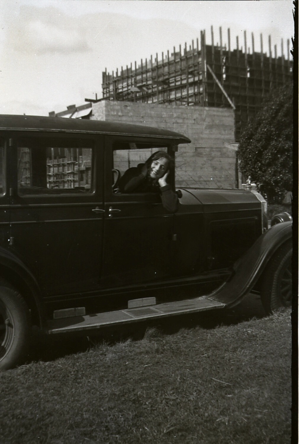 Young Woman at the Window of a Vintage Sedan, Construction Site Behind