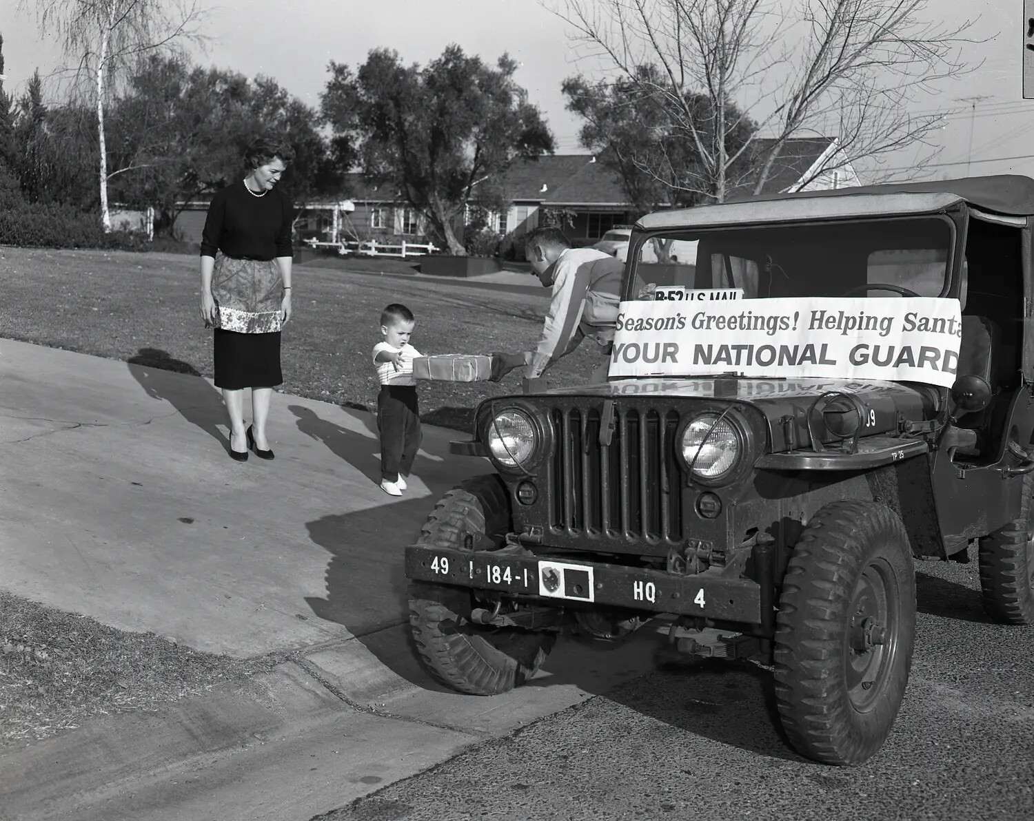 Close-Up View: National Guard Jeep and Guardsman Presenting Christmas Gift to Child, 'Helping Santa' Program, c. 1958-1962