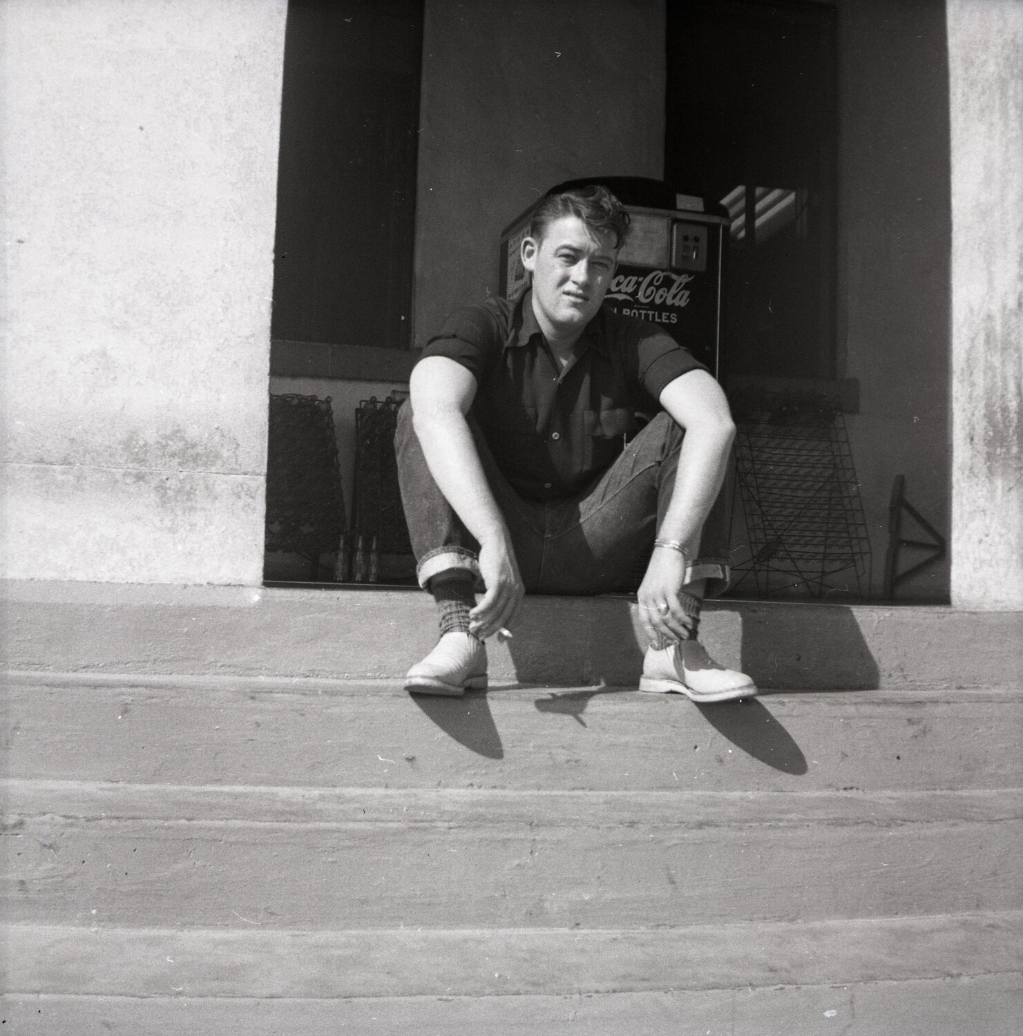 Young Man Seated on Steps Beside Vintage Coca-Cola Vending Machine