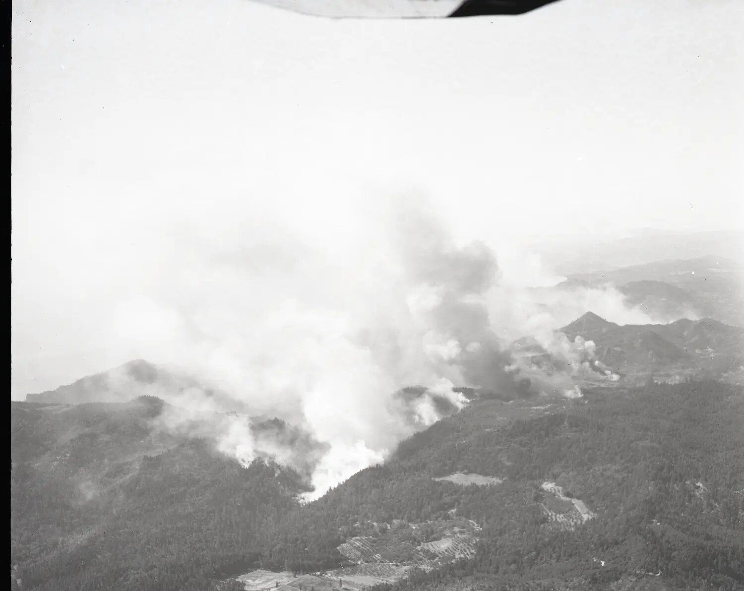 Aerial Reconnaissance Photograph of Wildfire Burning Across Forested Mountain Terrain