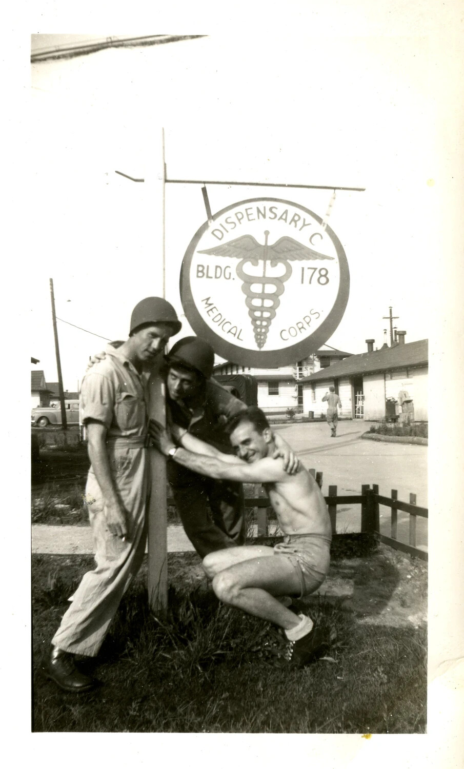 Three Servicemen Posing at Dispensary C Sign, Medical Corps, WWII Era Base