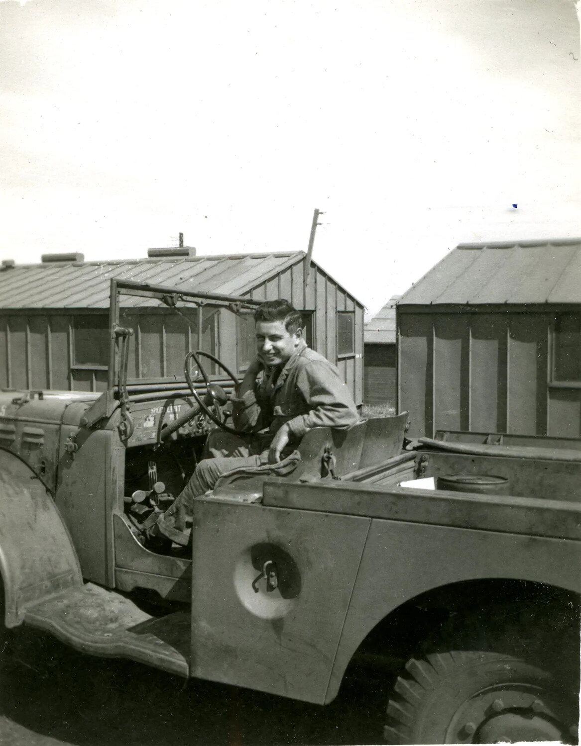Serviceman Seated in Military Utility Truck at Camp with Nissen Huts, 1946