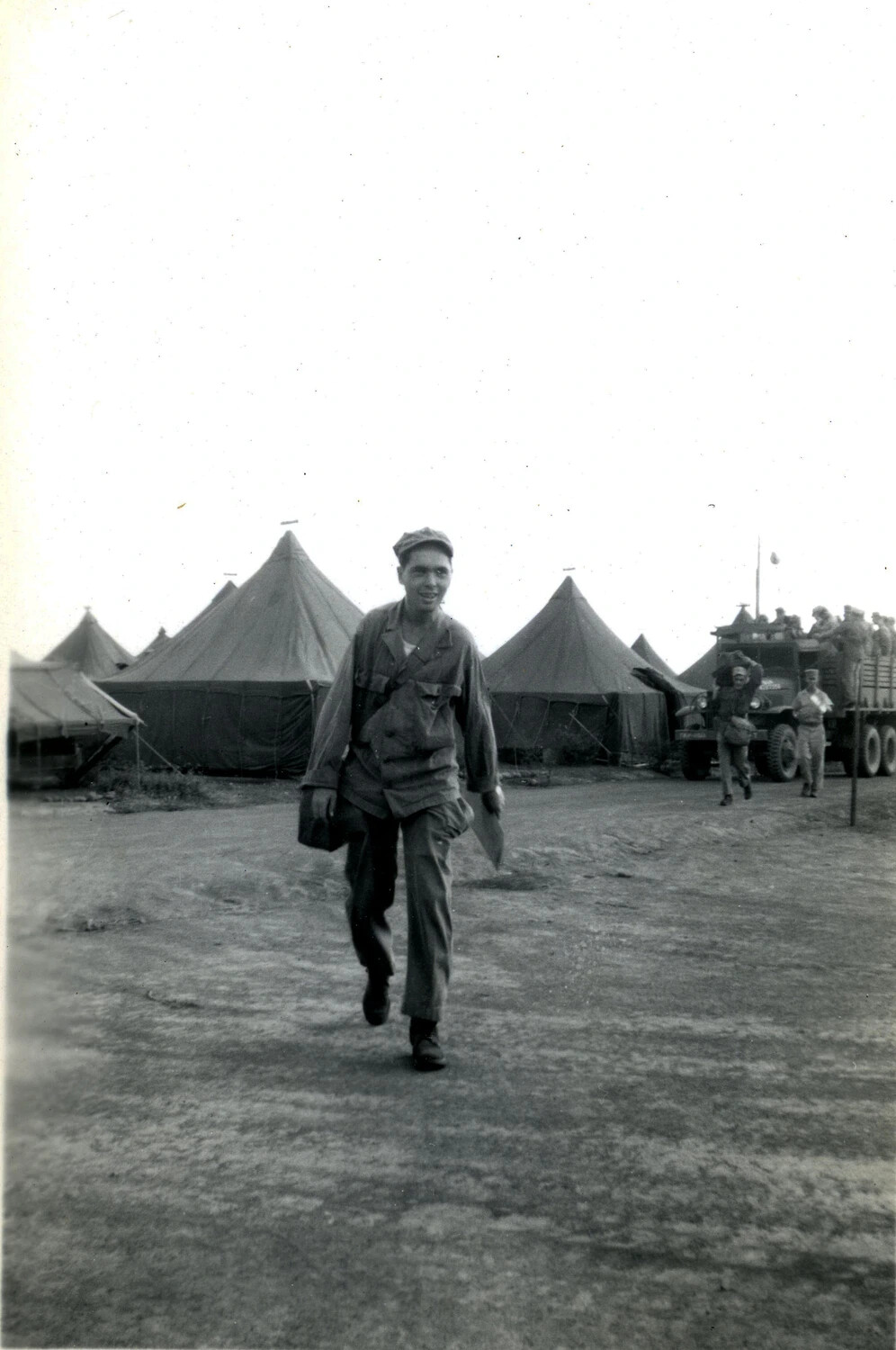 U.S. Marine Walking Through Tent Camp with Truck and Troops in Background, WWII