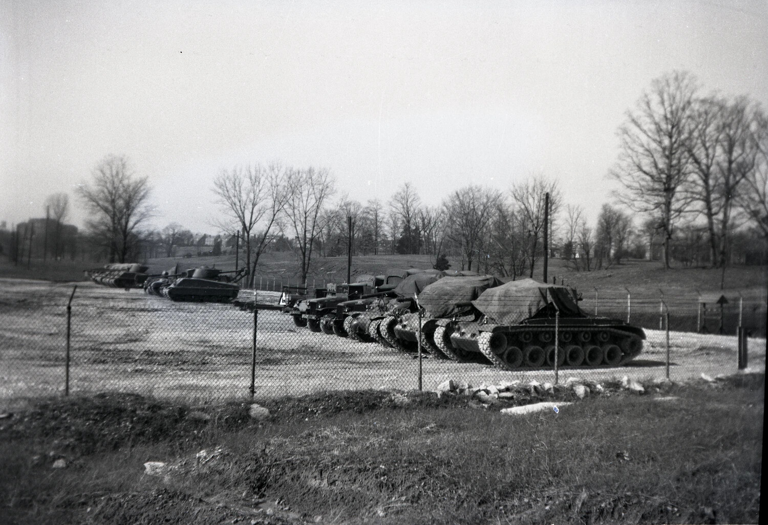 Row of Tarpaulin-Covered Medium Tanks in a Fenced Army Motor Pool