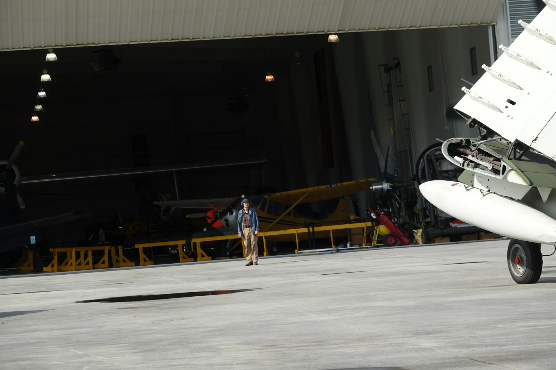 Museum Volunteer on Ramp with Yellow Liaison Aircraft in Hangar Background