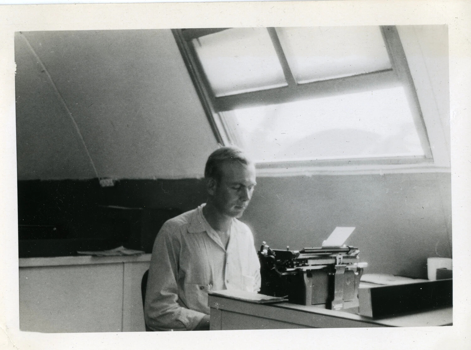 Serviceman Typing at Desk Beneath Skylight, Naval Air Station Office (VR-6 Agana, Guam Collection)