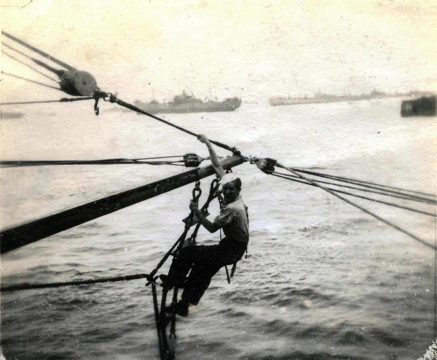 Sailor Working Cargo Boom Rigging Aboard Ship, Pacific Theater Harbor, WWII