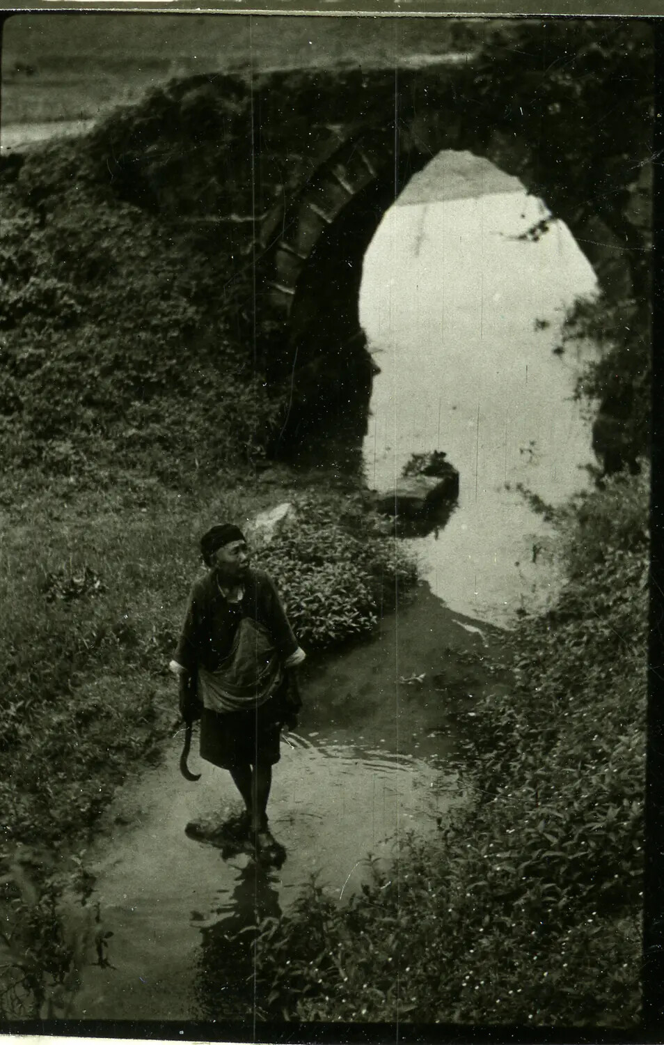 Elderly Local Man Wading Beneath Stone Arch Bridge, China-Burma Theater, WWII Era