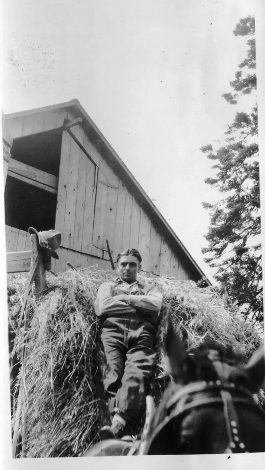 Young Man Reclining Atop a Hay Load, Low-Angle View of Barn