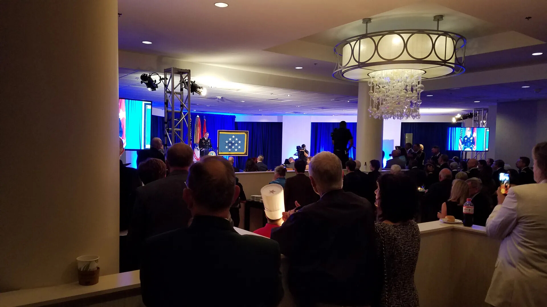 Crowd View of Formal Ceremony with Medal of Honor Flag Displayed on Stage