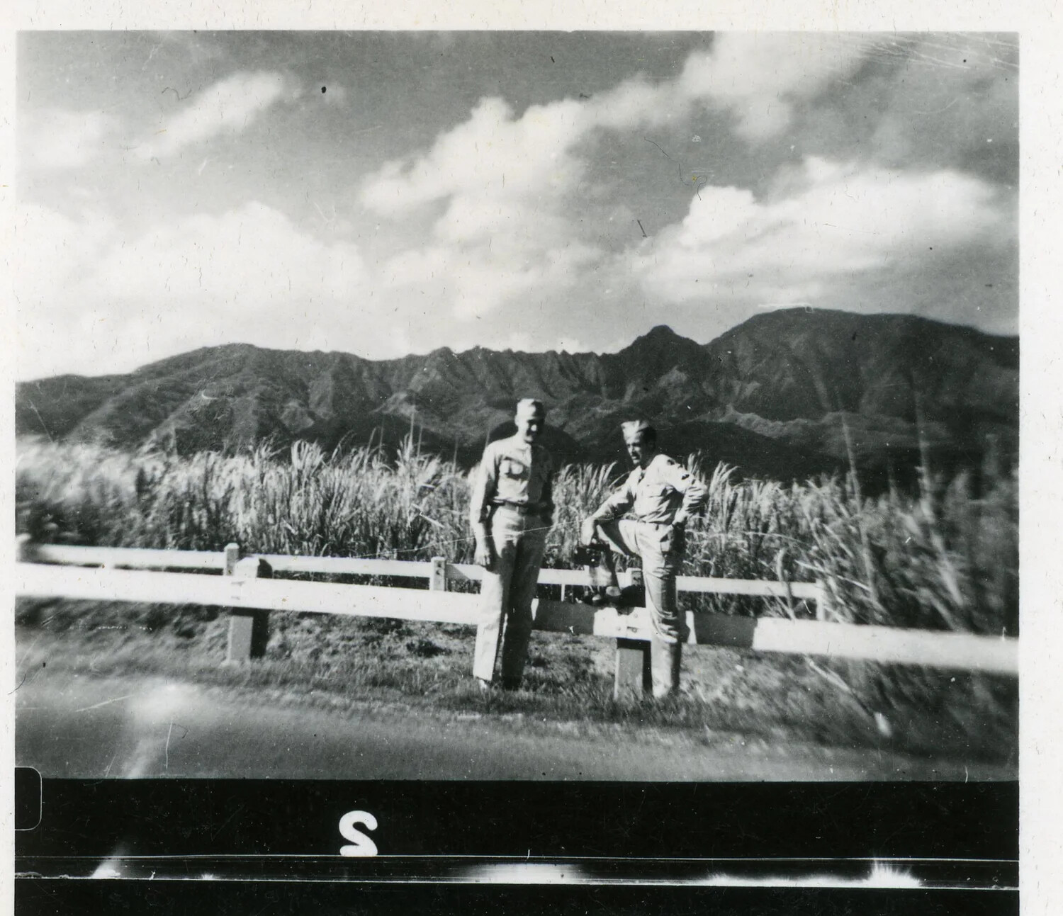 Two Servicemen at a Roadside Fence with Sugarcane Fields and Mountains, Hawaii, WWII Era
