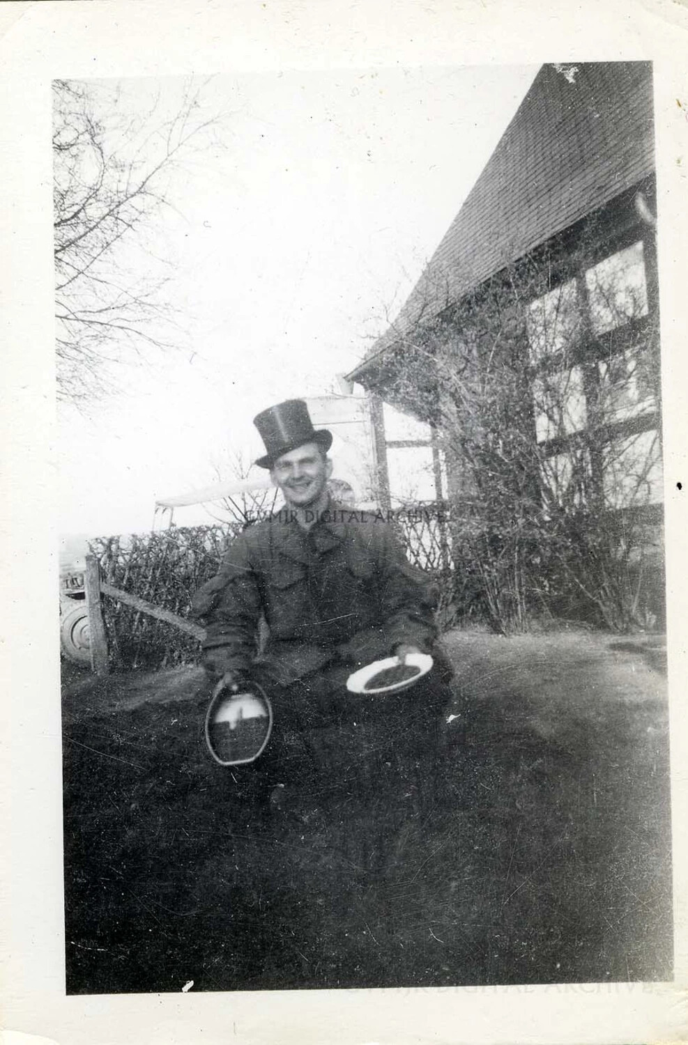 101st Airborne Division Soldier Clowning in Civilian Top Hat with M1 Helmet in Hand, Rural European Farmhouse, WWII