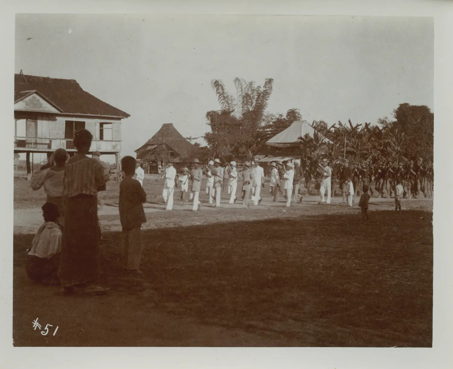 American Military Band and Troop Column Marching Through Philippine Village, with Local Onlookers