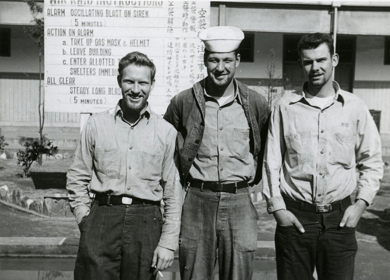 Three U.S. Navy Sailors in Front of Bilingual Air Raid Instructions Sign, Japan, Korean War Era