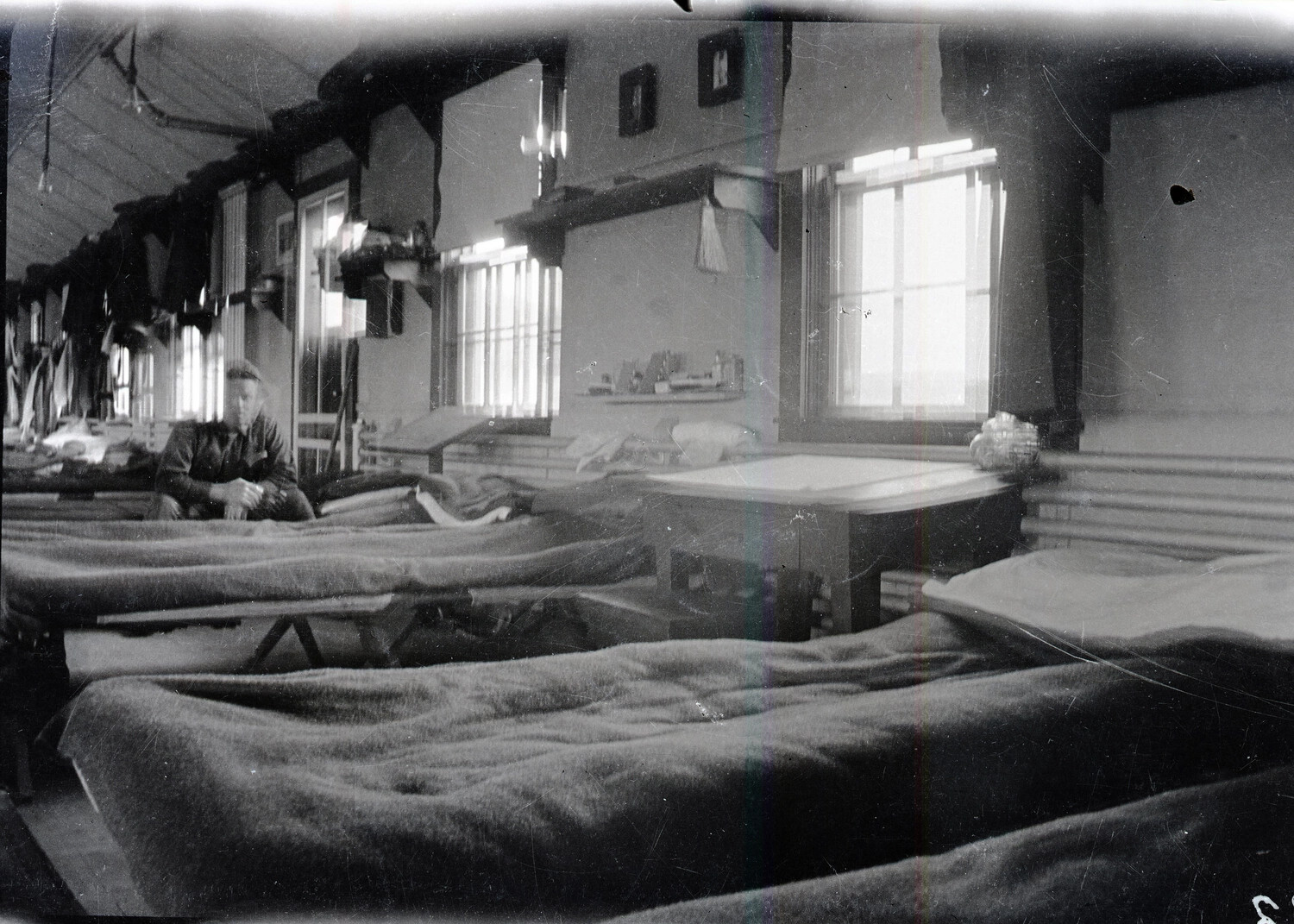 Interior of a WWI-Era Barracks or Billet in France Showing Rows of Cots and a Soldier at Rest