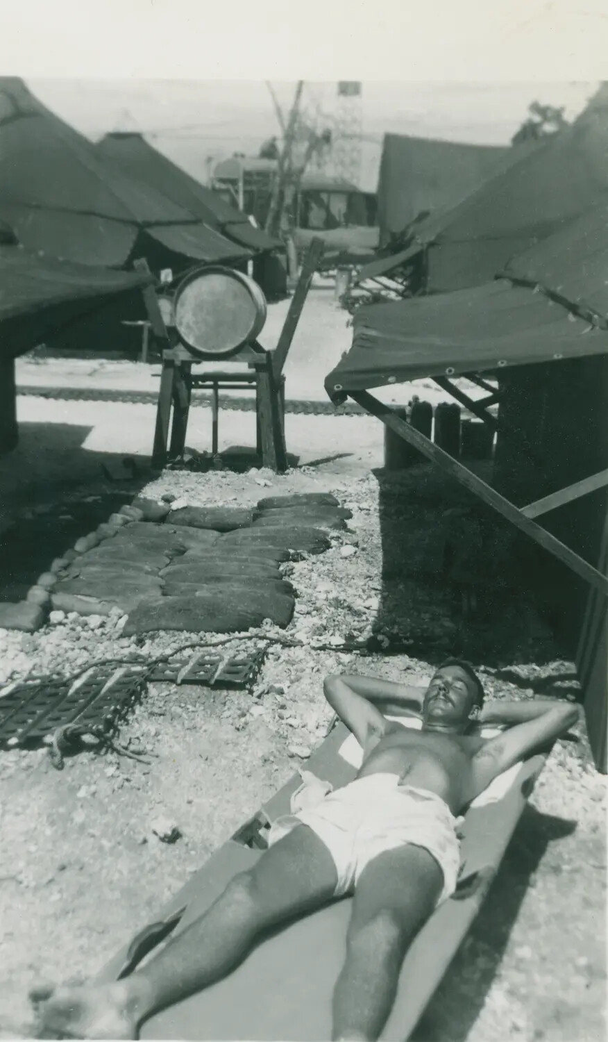 Serviceman Sunbathing on a Cot at a Forward Base Camp