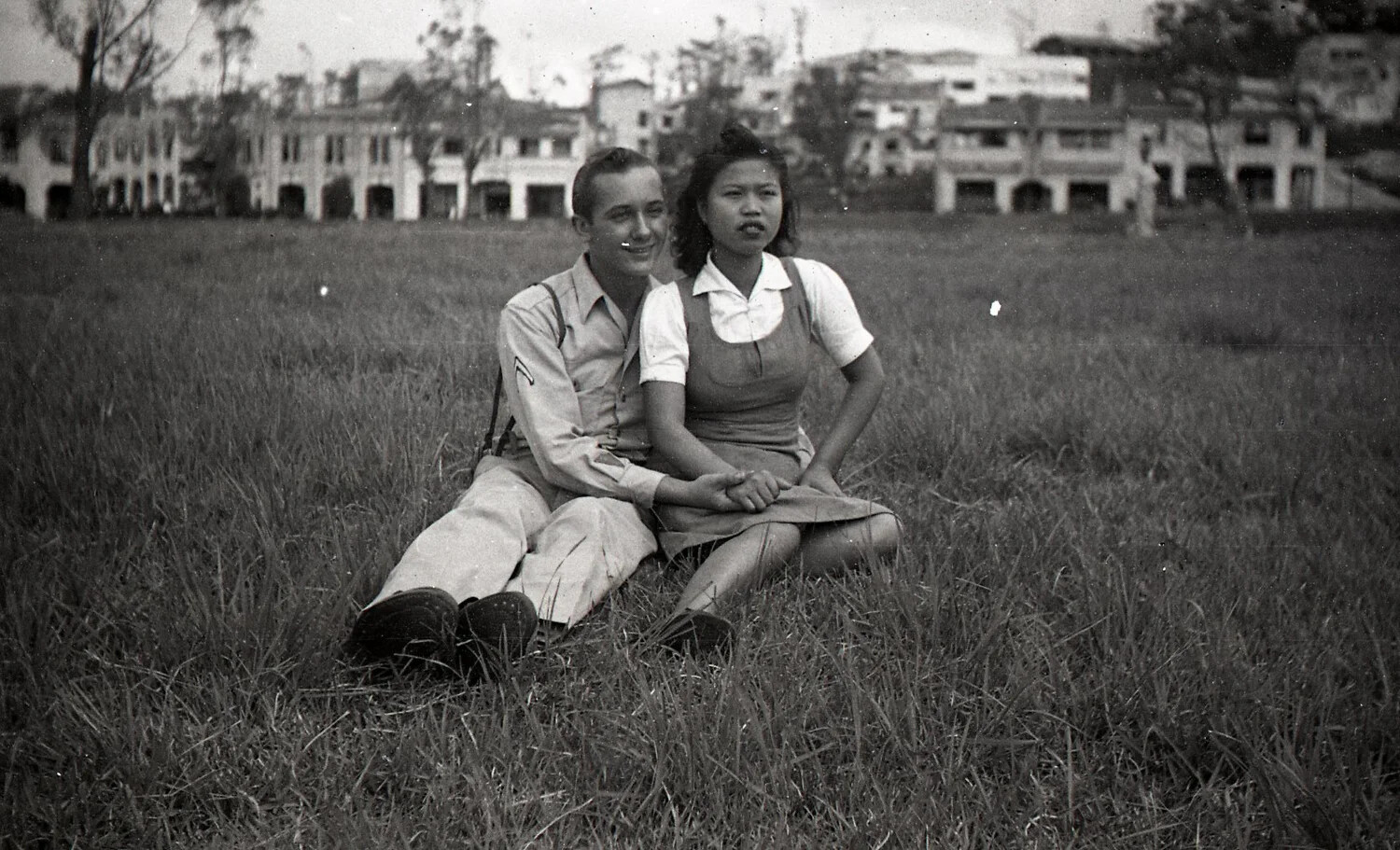 American Serviceman and Filipina Companion Seated in a Field Near War-Damaged Buildings, Luzon, Philippines, WWII Era