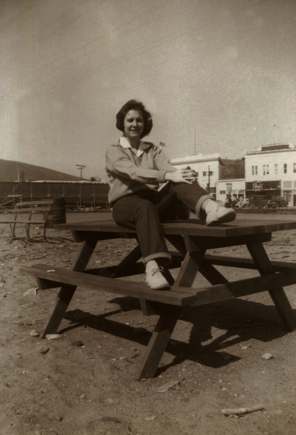 Young Woman Seated on Picnic Table, Small-Town Main Street Backdrop
