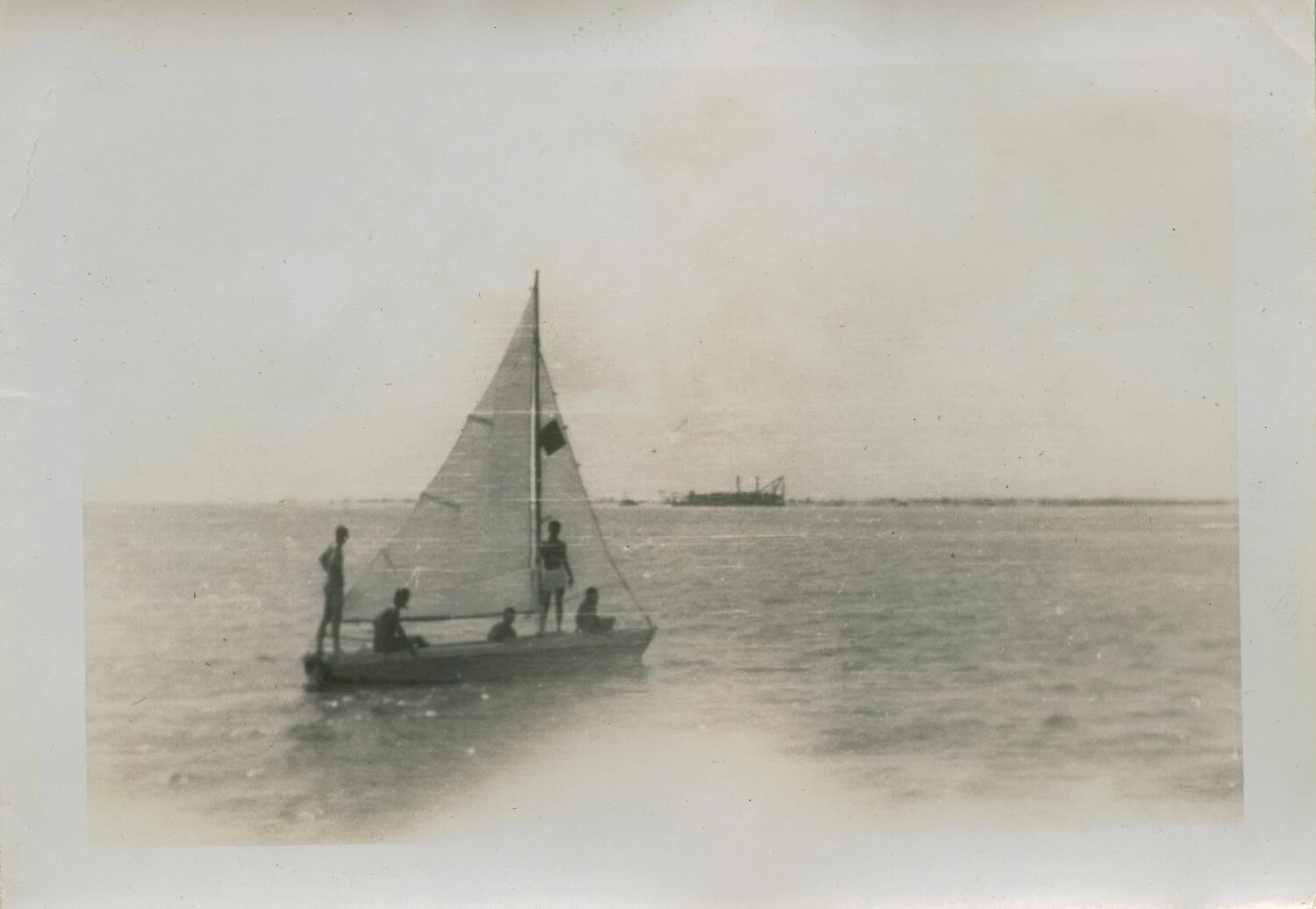 Small Sailboat with Four Passengers on Open Water, Distant Work Vessel on Horizon