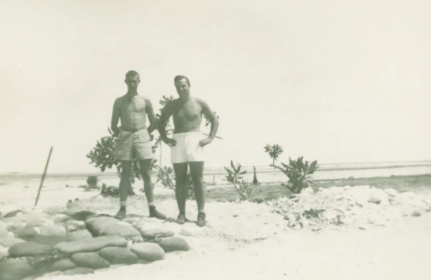 Two Servicemen on Coral Beach Beside Sandbag Revetment, Pacific Island Base, WWII