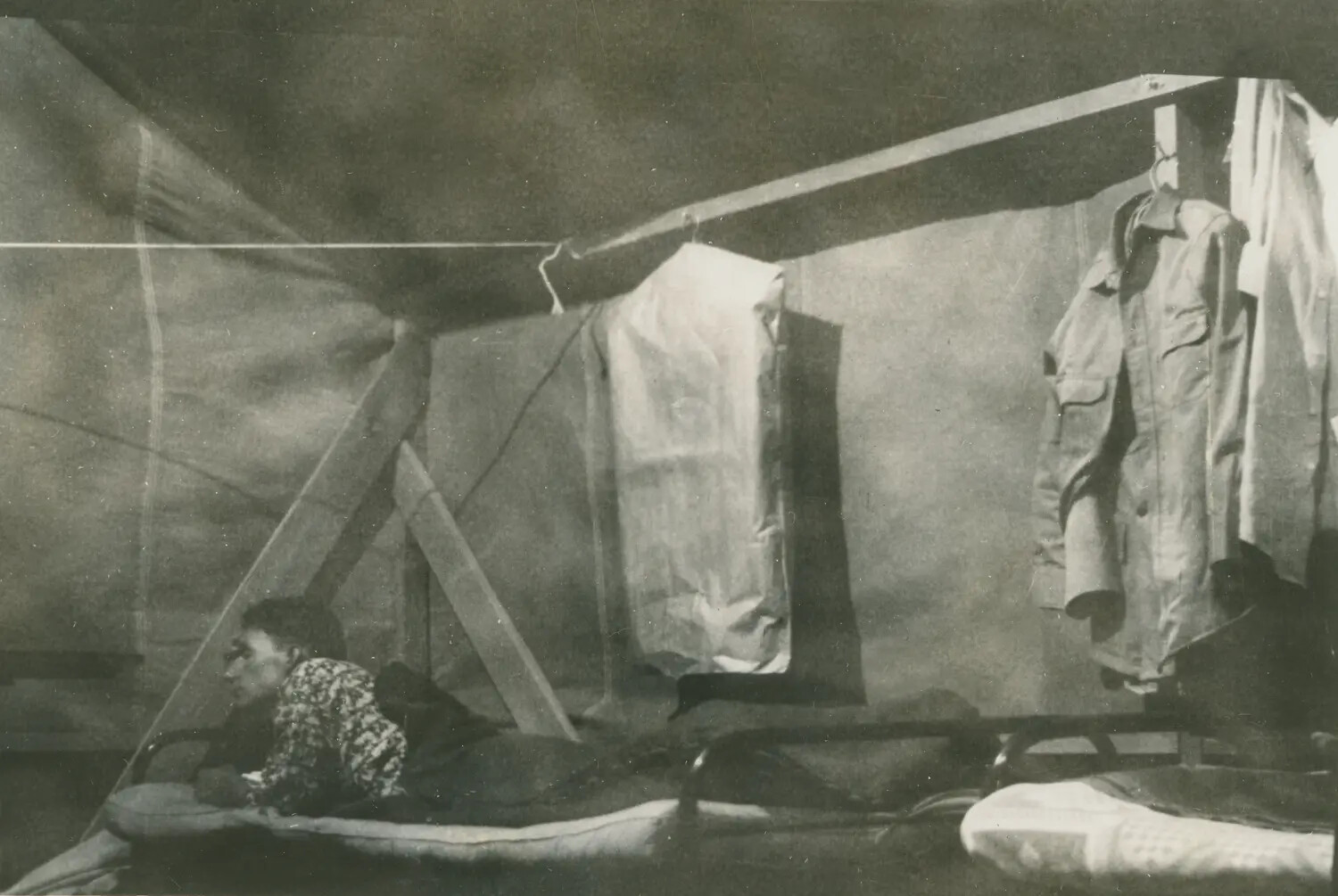 Interior of Military Tent Quarters with Hanging Uniforms and Serviceman on Cot