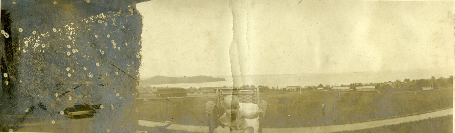 Infant in Wicker Chair Overlooking Coastal Settlement, Philippines, Early 1900s (Damaged Print)