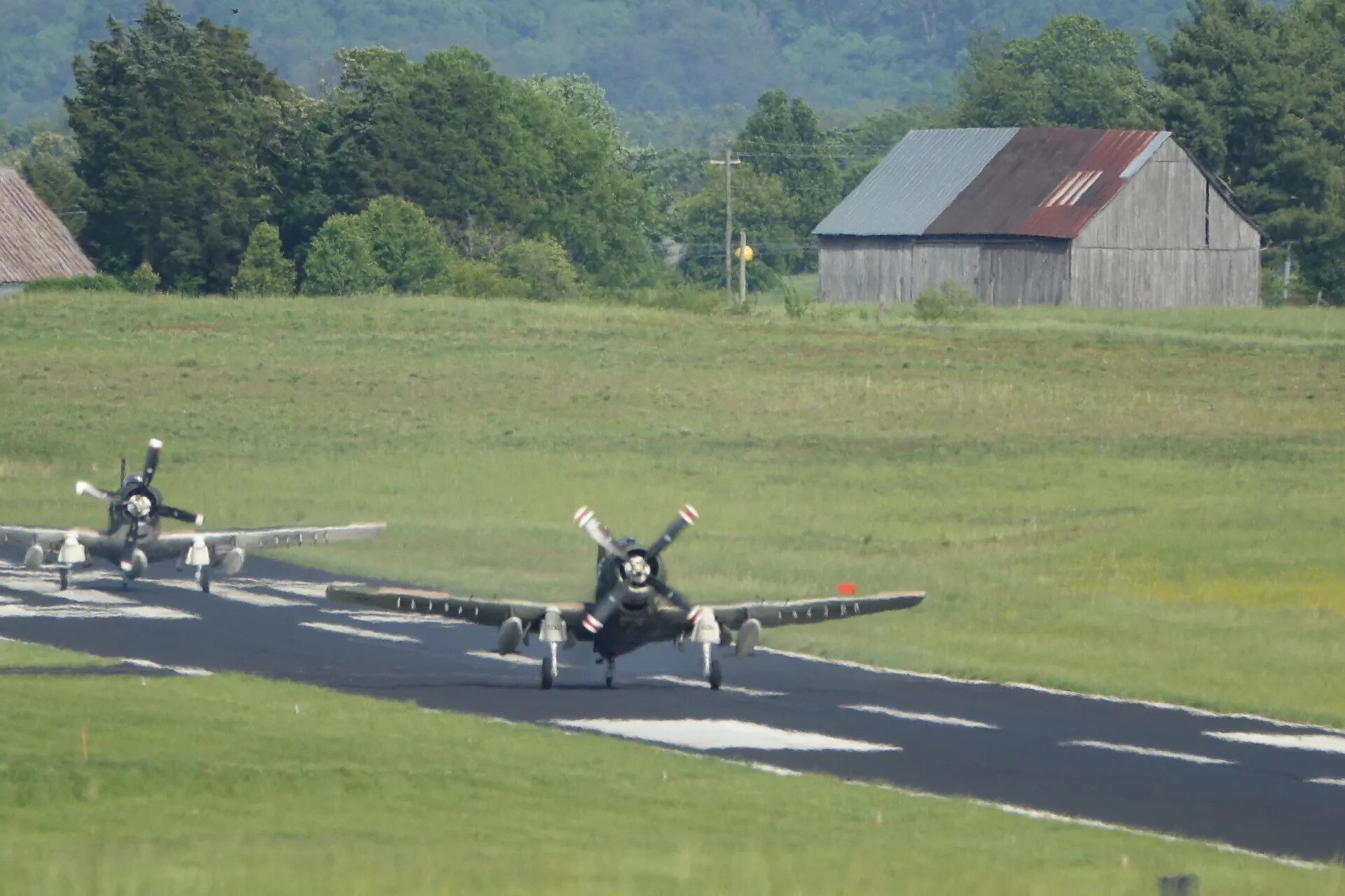 Pair of A-1 Skyraiders Taxiing Past a Rural Barn, Head-On Telephoto View