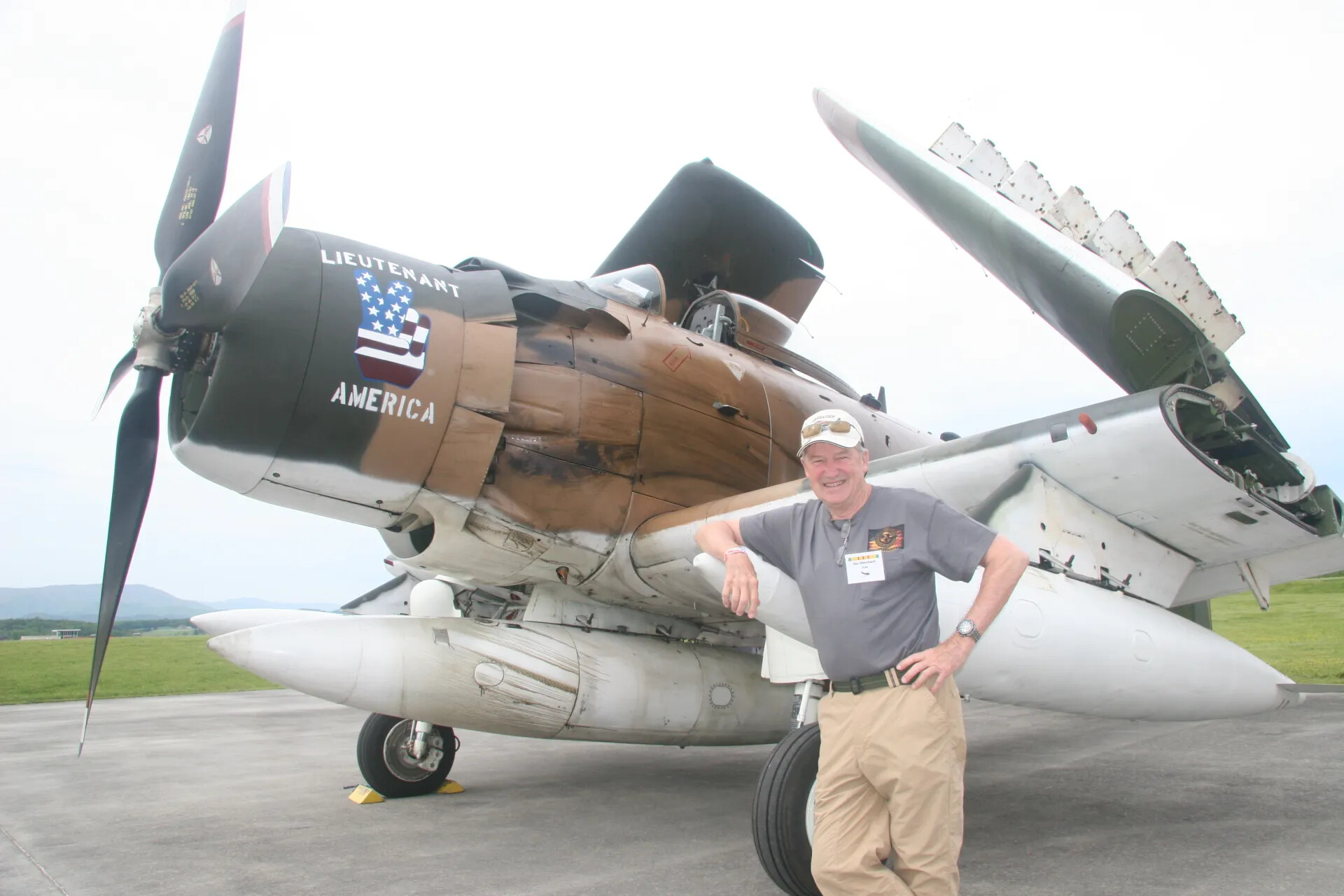 Attendee Posing with Douglas A-1 Skyraider 'Lieutenant America' Nose Art, Outdoor Airfield