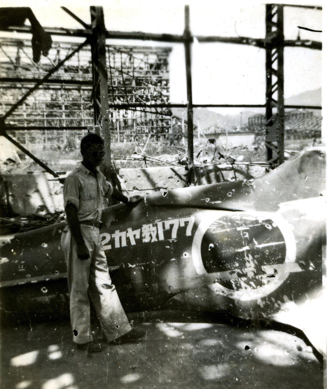 American Serviceman Posing with Wrecked Japanese Aircraft in Bombed Hangar Ruins
