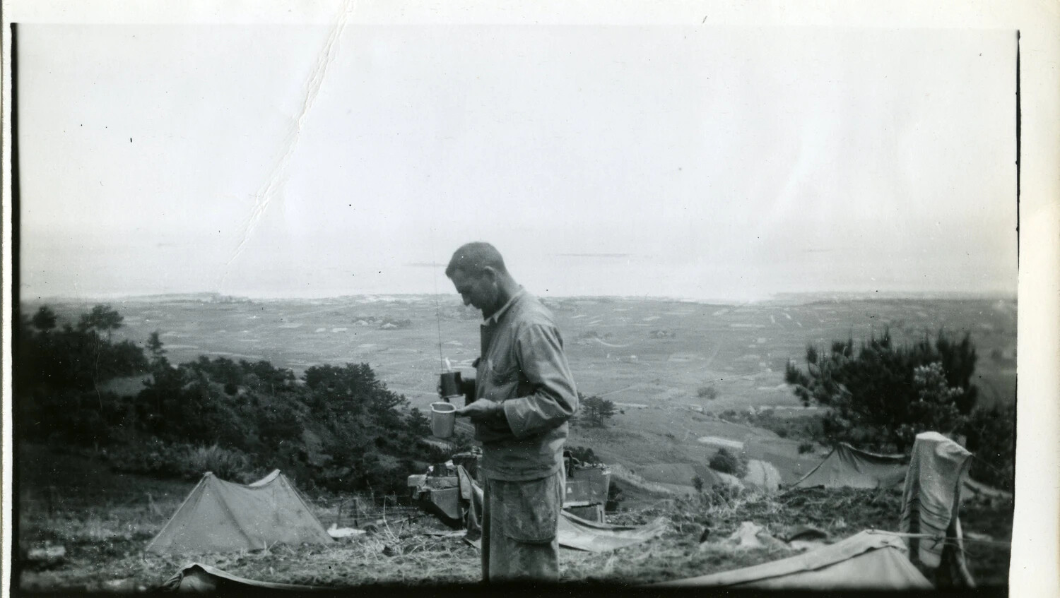 Serviceman Preparing a Drink at Hilltop Bivouac Overlooking Coastal Valley, Likely Okinawa, 1945